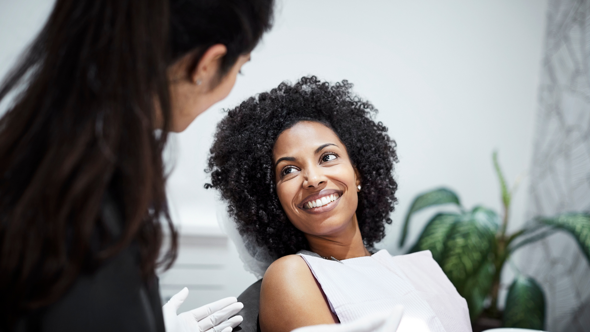 A woman smiling while sitting in a dental chair during a dental appointment with a female dentist.