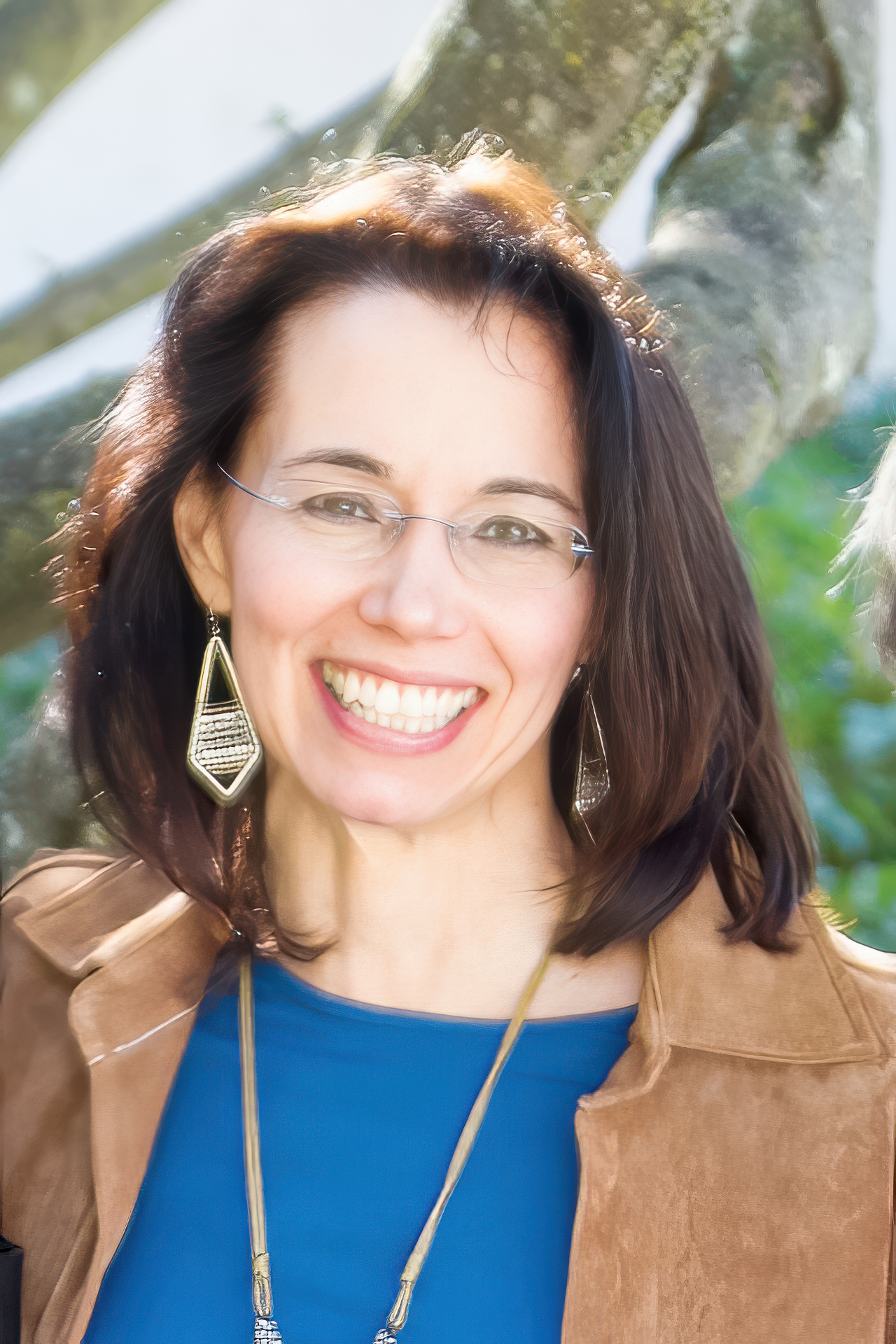 Happy woman with brown hair, glasses, and earrings, smiling outdoors.