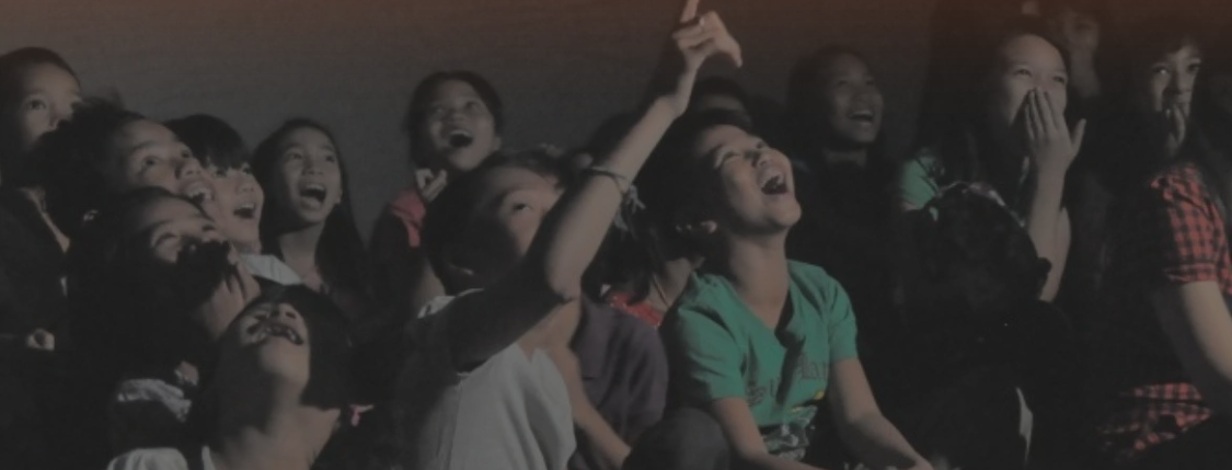 Group of children laughing and enjoying a performance or show in a dark room.