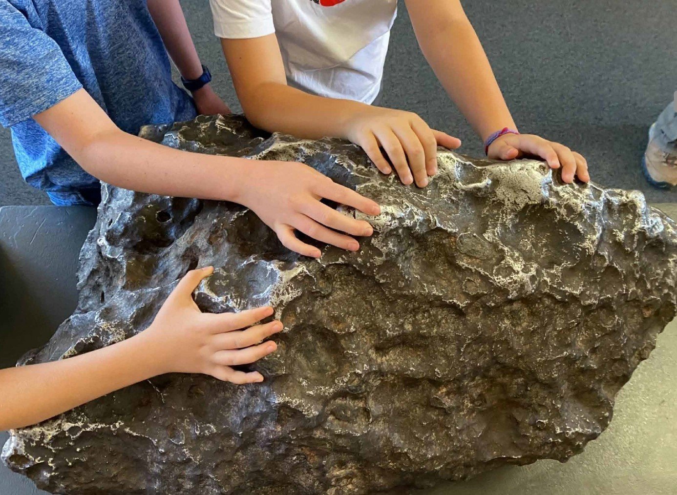 Children touching a large, textured rock.