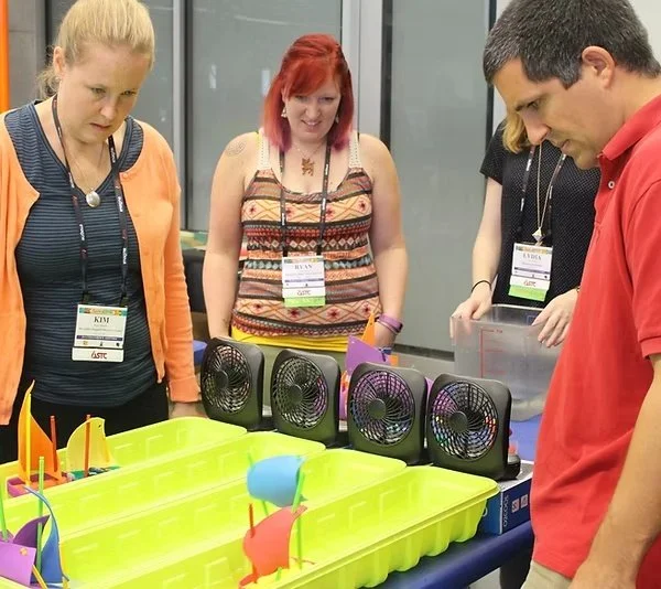 Teachers observing a tabletop science experiment with colorful objects and fans at a conference. at the Meteor Crater Education Alliance STEM training program.