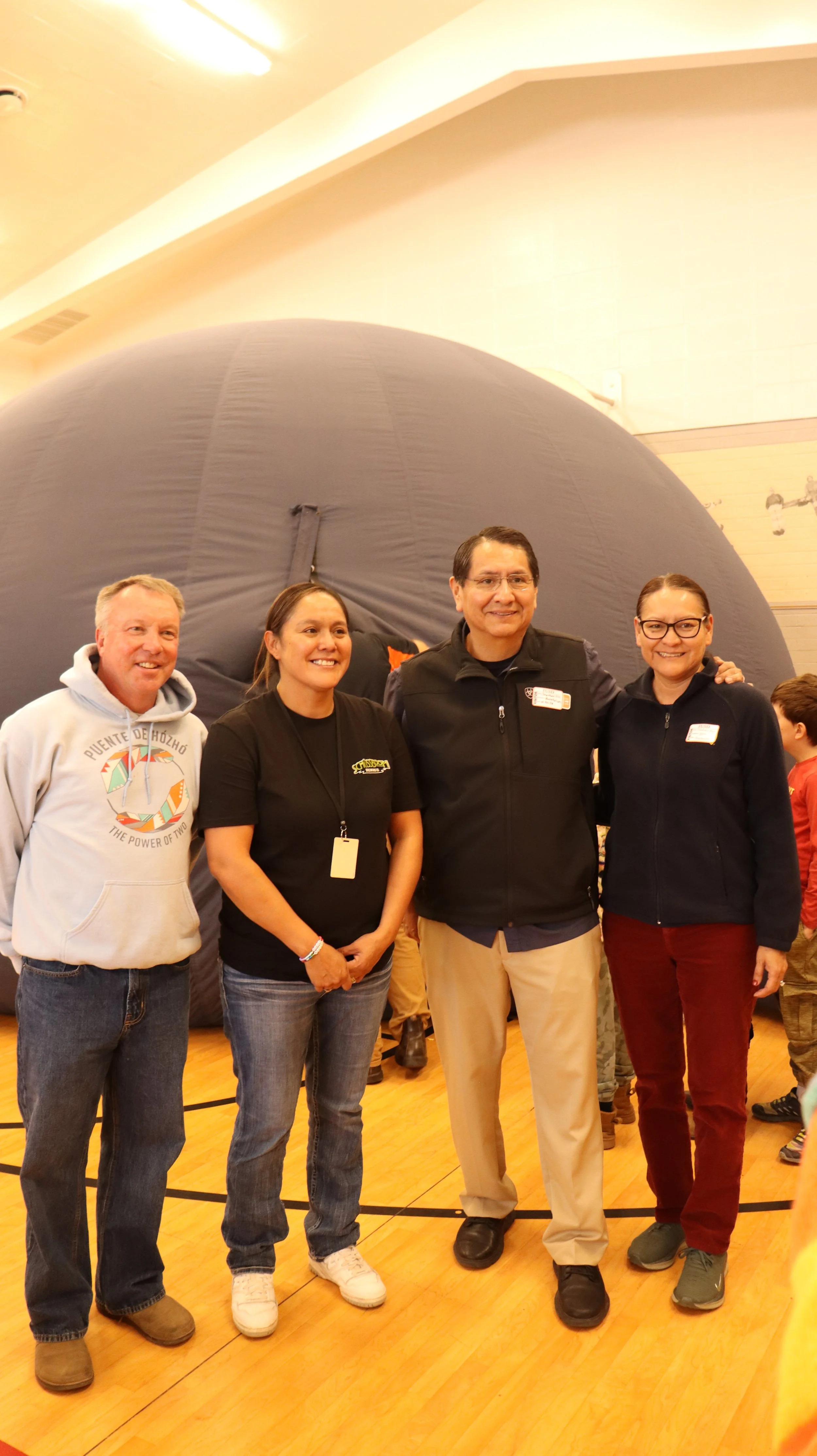 Four people standing in front of a large, gray, spherical object indoors, smiling at the camera.