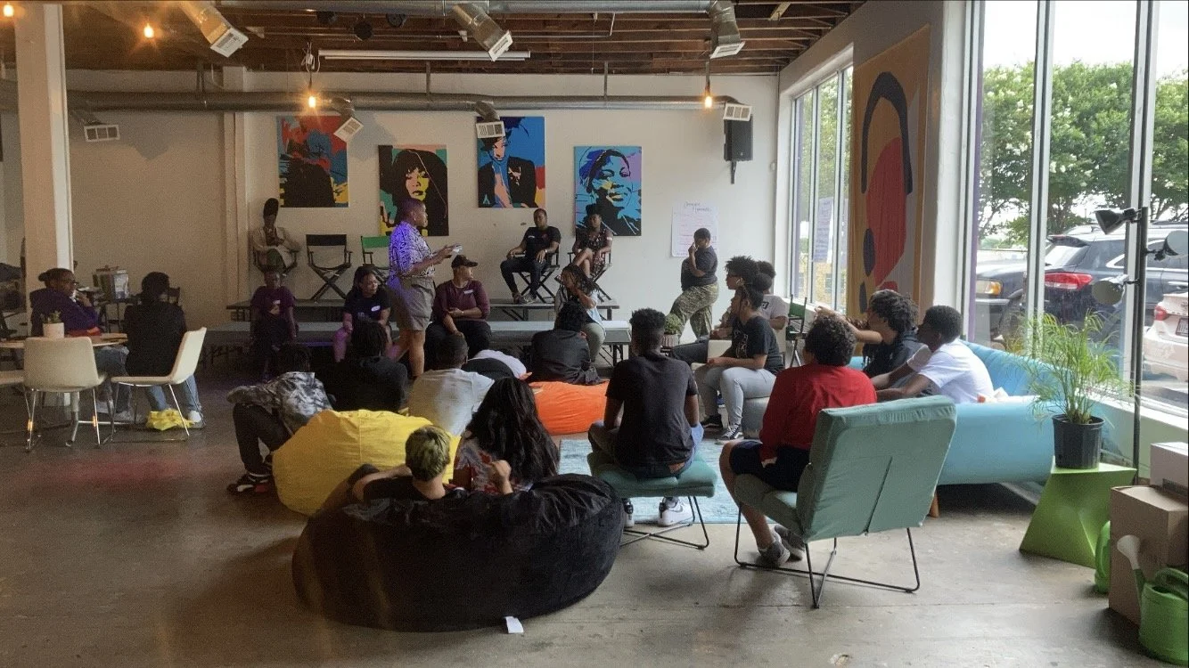 Group of people attending a discussion or presentation in a modern, art-filled event space with large windows and colorful artwork on the walls.