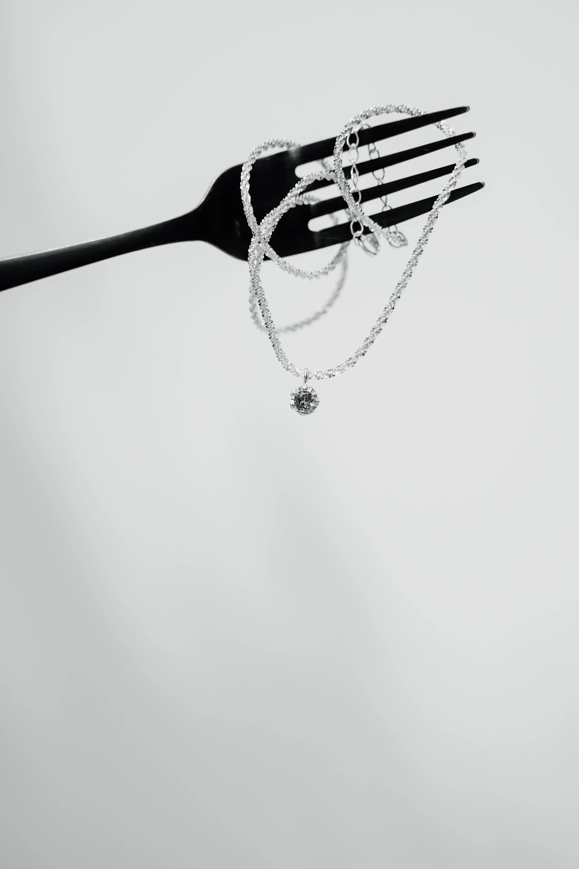 Silver jewelry, including a necklace with a large central stone, a bracelet, and earrings, displayed on a black fork.