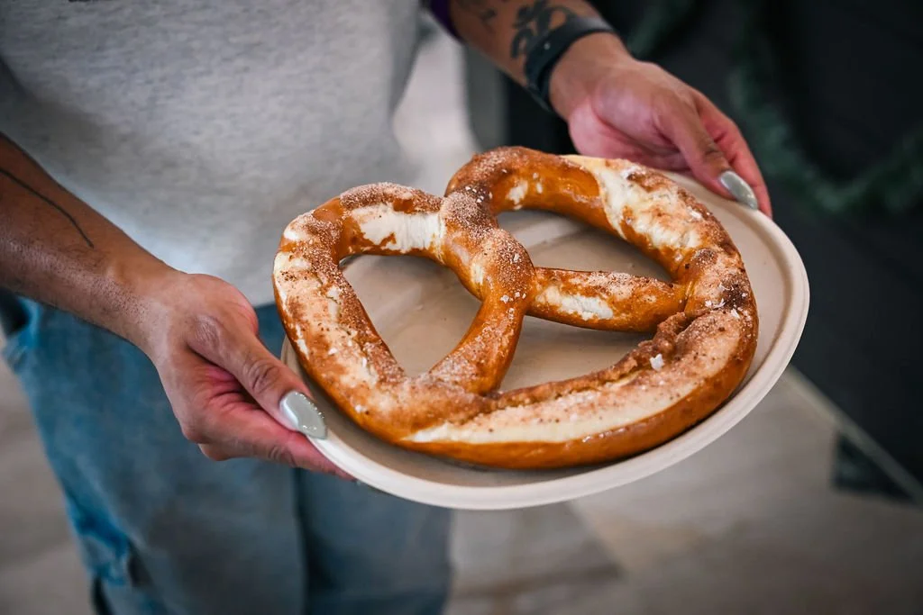 Person holding a plate with two large soft pretzels, sprinkled with coarse salt.