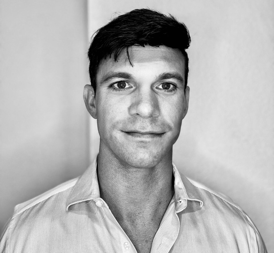 Black and white photo of a man with short dark hair wearing a collared shirt, looking at the camera.