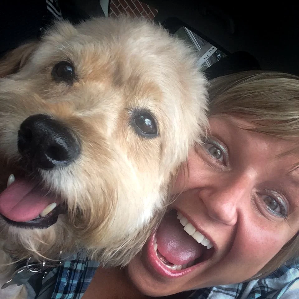 A woman and a golden retriever dog are close together, both smiling and looking at the camera.