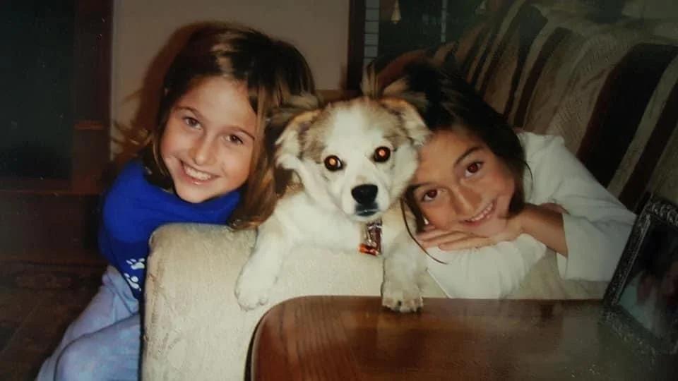 Two young girls and a dog sitting at a table in a cozy home setting.