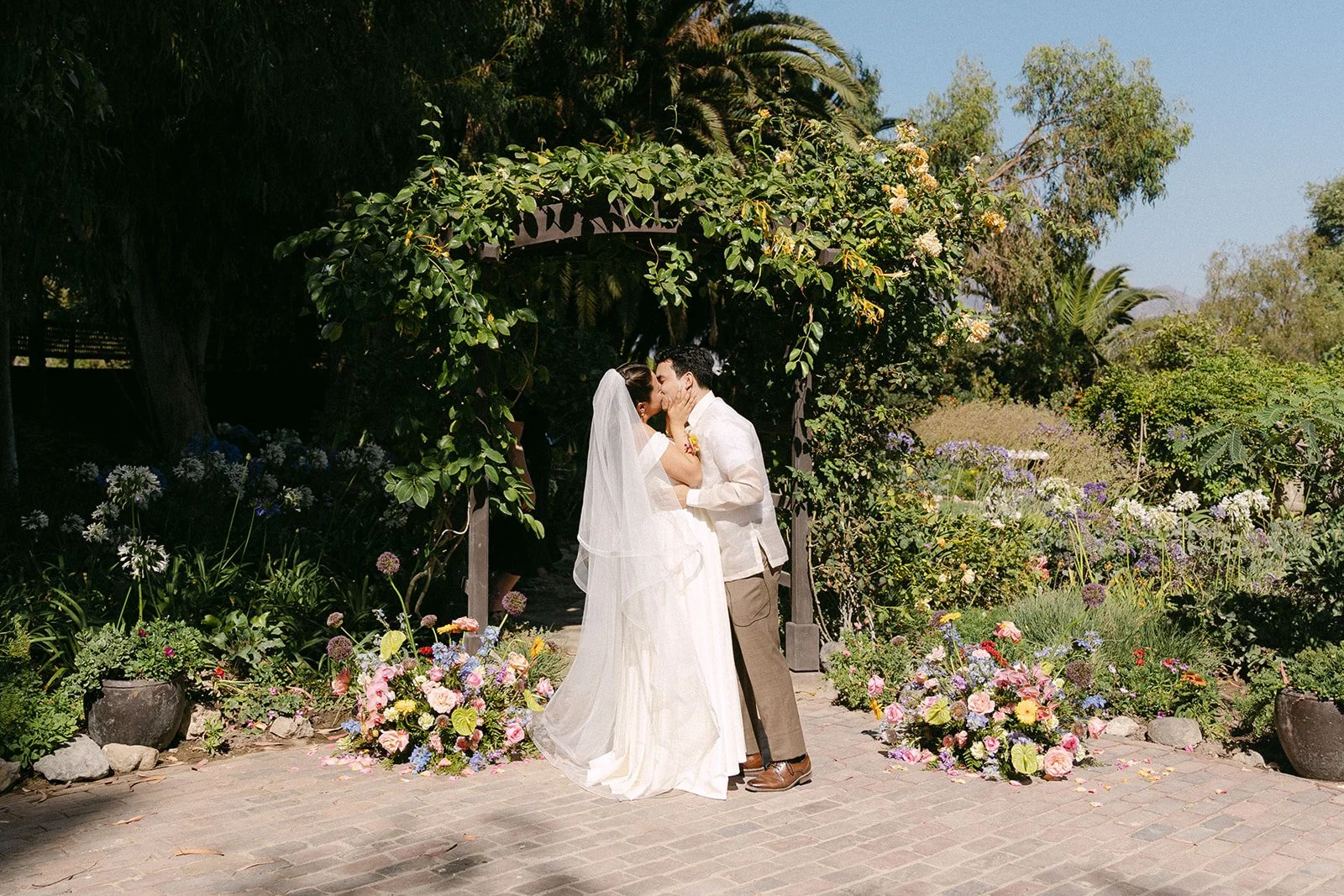 A couple has their first kiss after eloping in the lush gardens at McCormick Home Ranch.