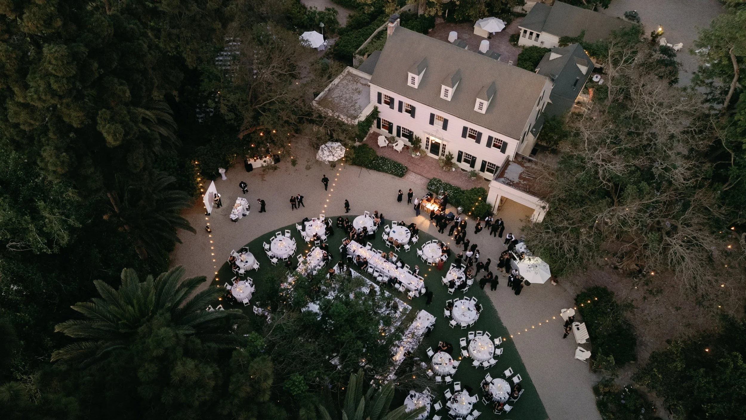 Aerial view of white linen tables decorated with candles and flowers, a photo booth and buffet at McCormick Home Ranch for a black tie event.