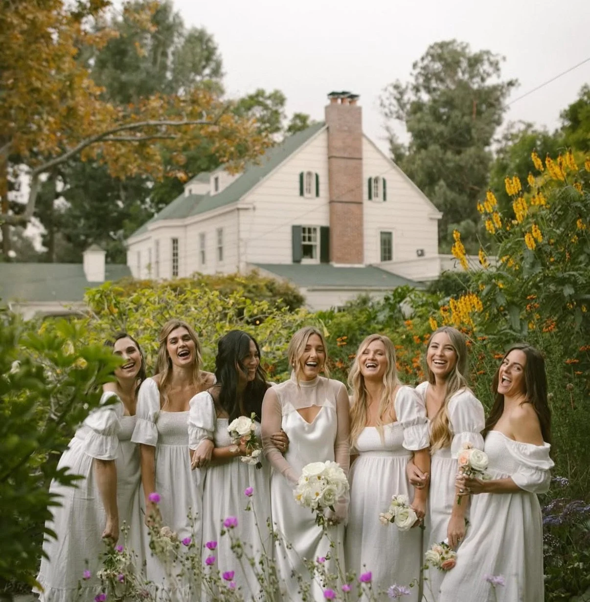 Bride and her bridal party giggling holding flowers in front of McCormick Home Ranch.