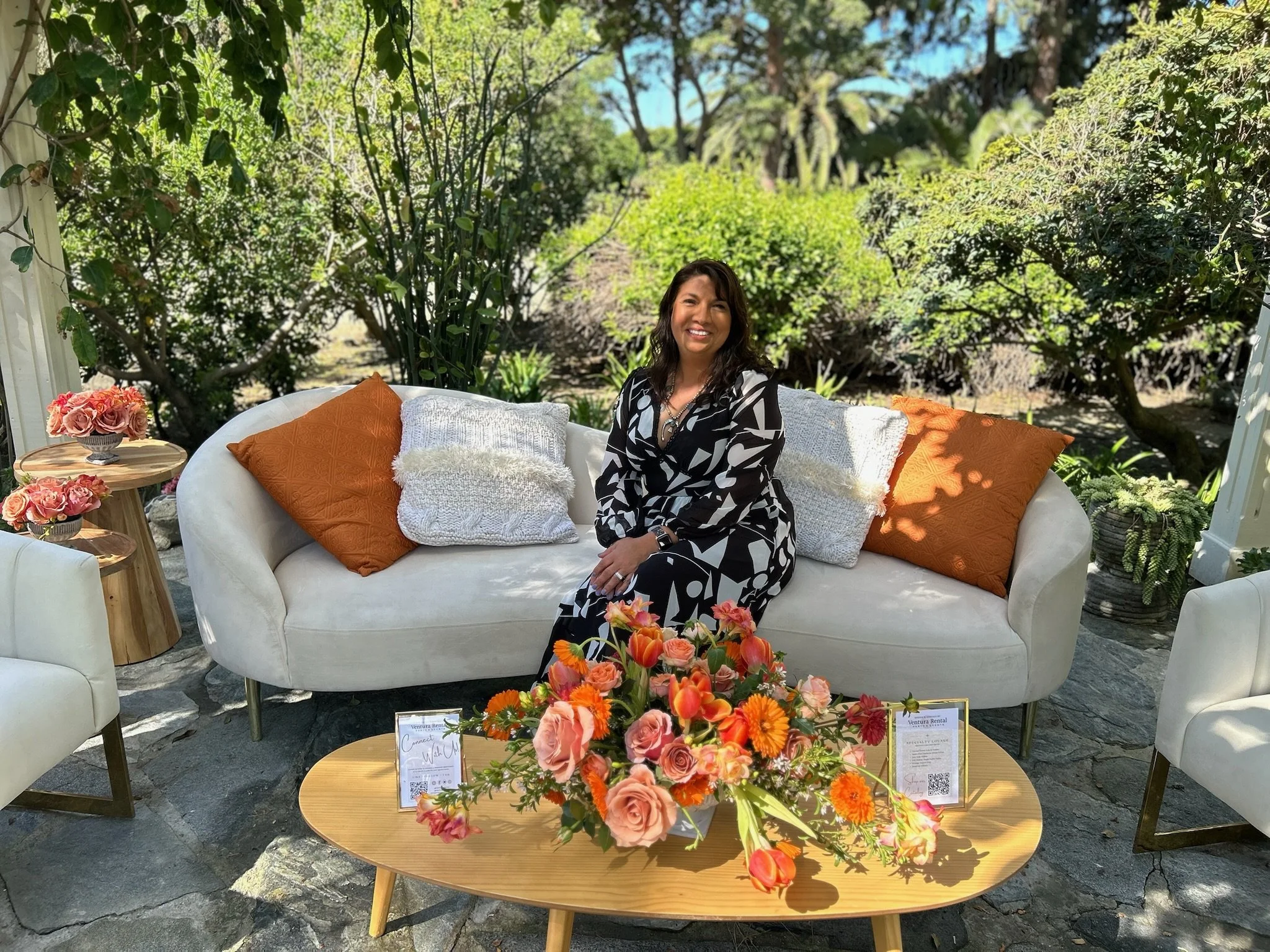 Becky our on site manager smiling while sitting amongst our garden with an orange flower arrangement in front of her.