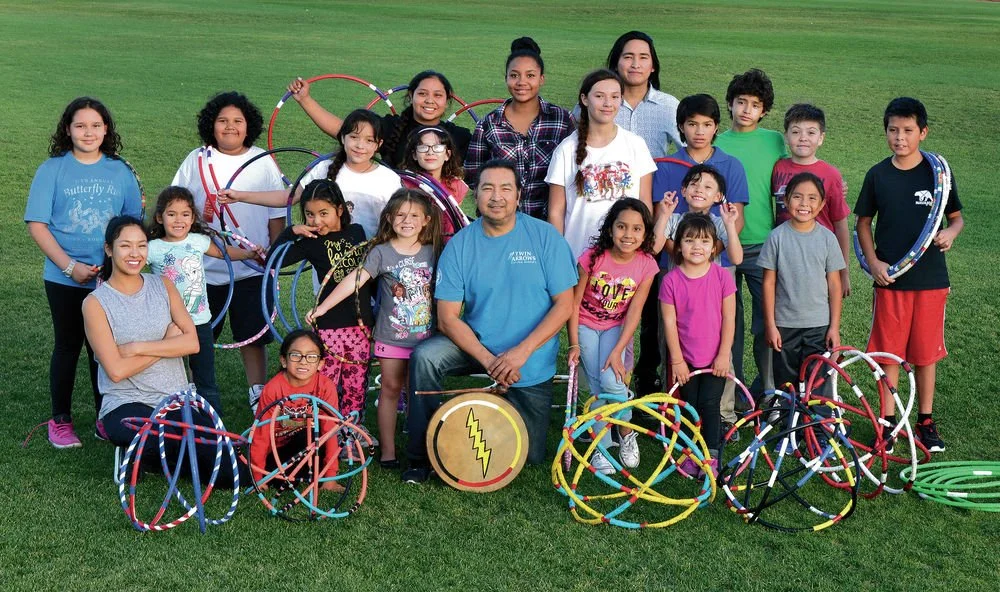Group of children and a man outdoors on a grassy field with colorful hula hoops