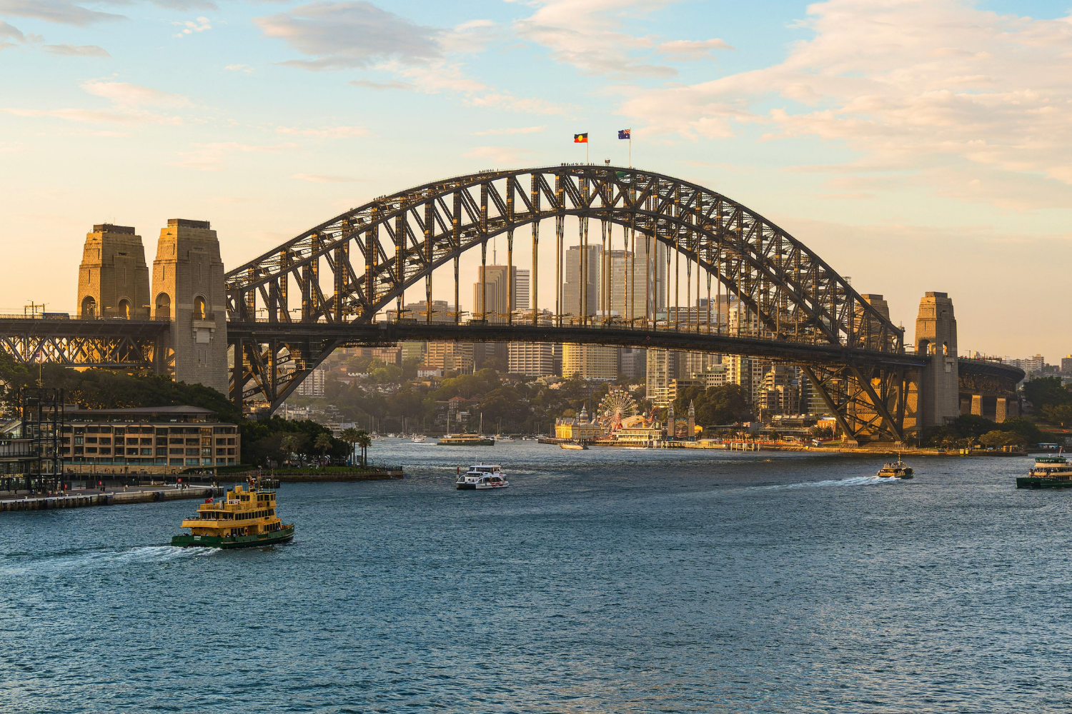 View of the Sydney Harbour Bridge during sunset with boats on the water and city skyline in the background.