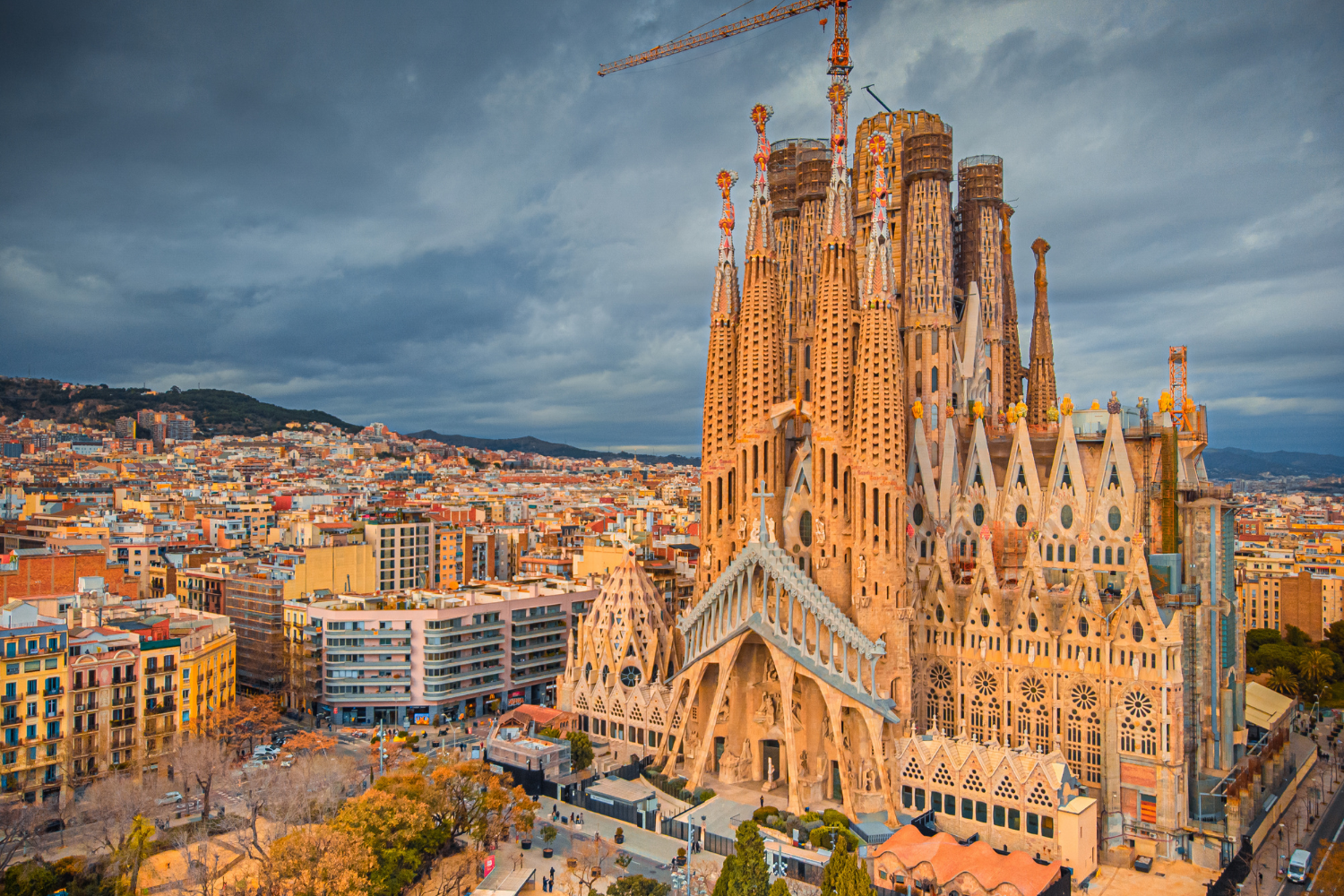 Aerial view of the Sagrada Familia basilica under construction in Barcelona, Spain, with surrounding cityscape and cloudy sky.