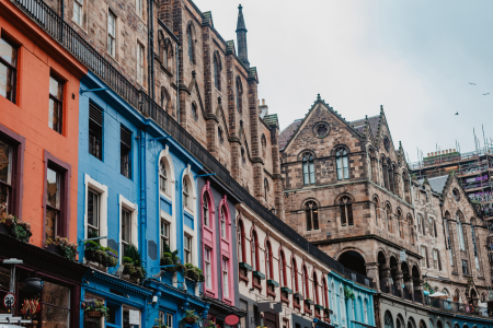 Colorful row of buildings with vibrant facades in orange, blue, pink, and green in front of a historic stone church or cathedral.