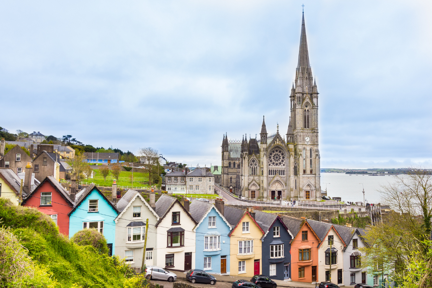 Colorful houses in front of a large Gothic-style church with a tall spire by the waterfront
