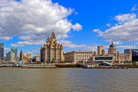 View of a city skyline with historic and modern buildings along a river, under a partly cloudy sky.