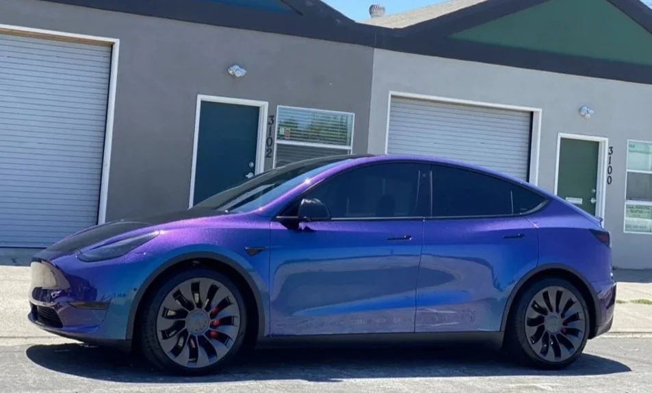 A shiny blue Tesla Model Y parked outside a gray building with blue doors and windows.