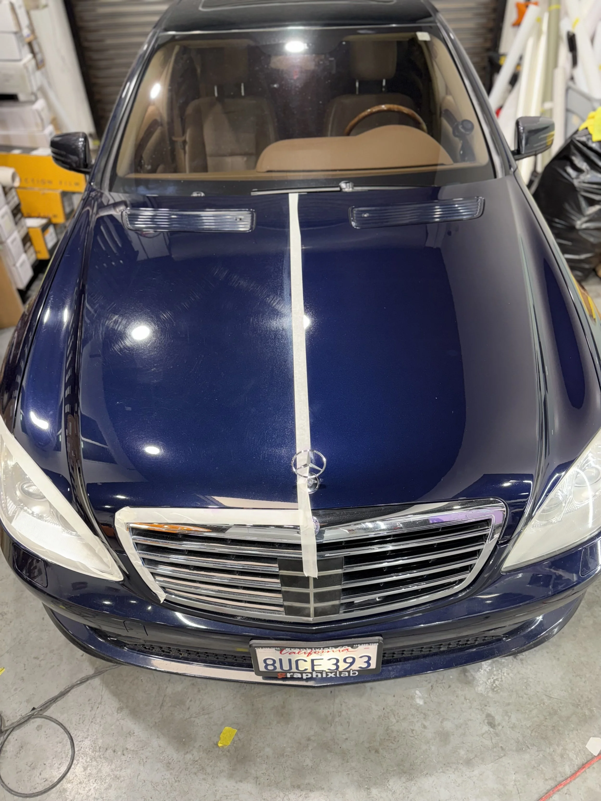 Front view of a dark blue Mercedes-Benz car with a white stripe running down the center of the hood, parked in a garage.