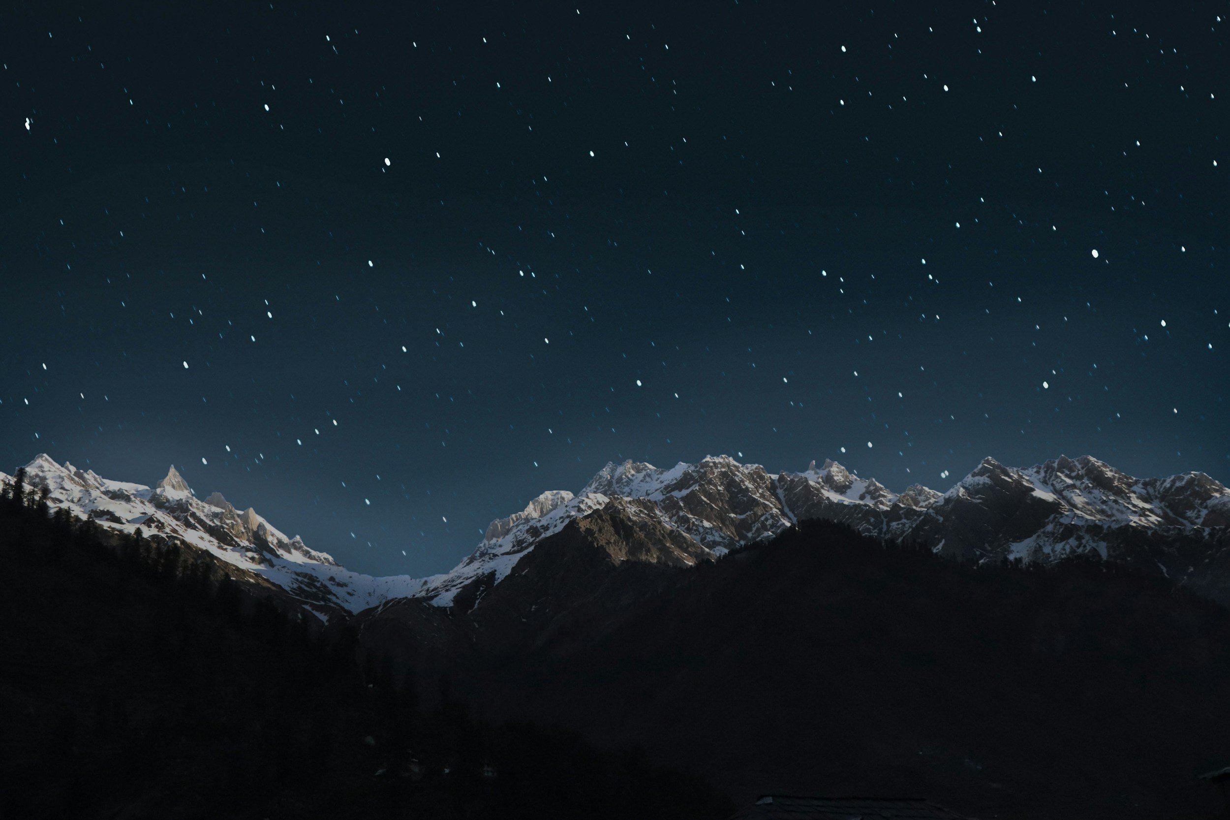 Nighttime mountain landscape with snow-covered peaks and a starry sky.