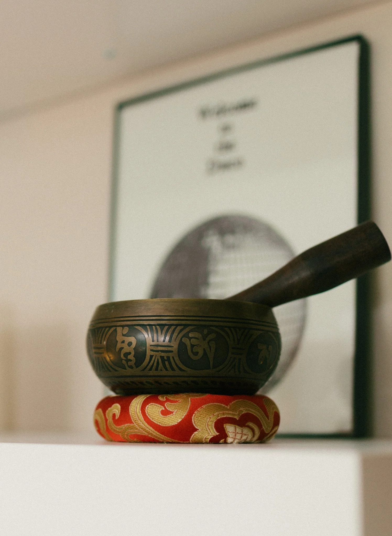 Stacked Tibetan singing bowls with a black and gold bowl on top of red and gold bowls, against a blurred background.
