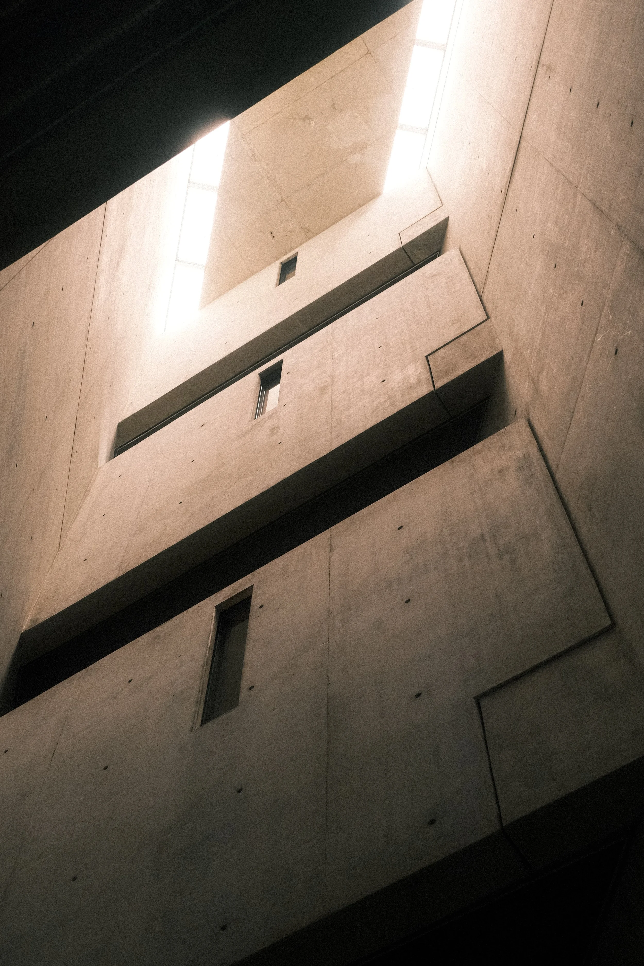 Interior view of a modern building's concrete walls and large windows with natural light coming from above.