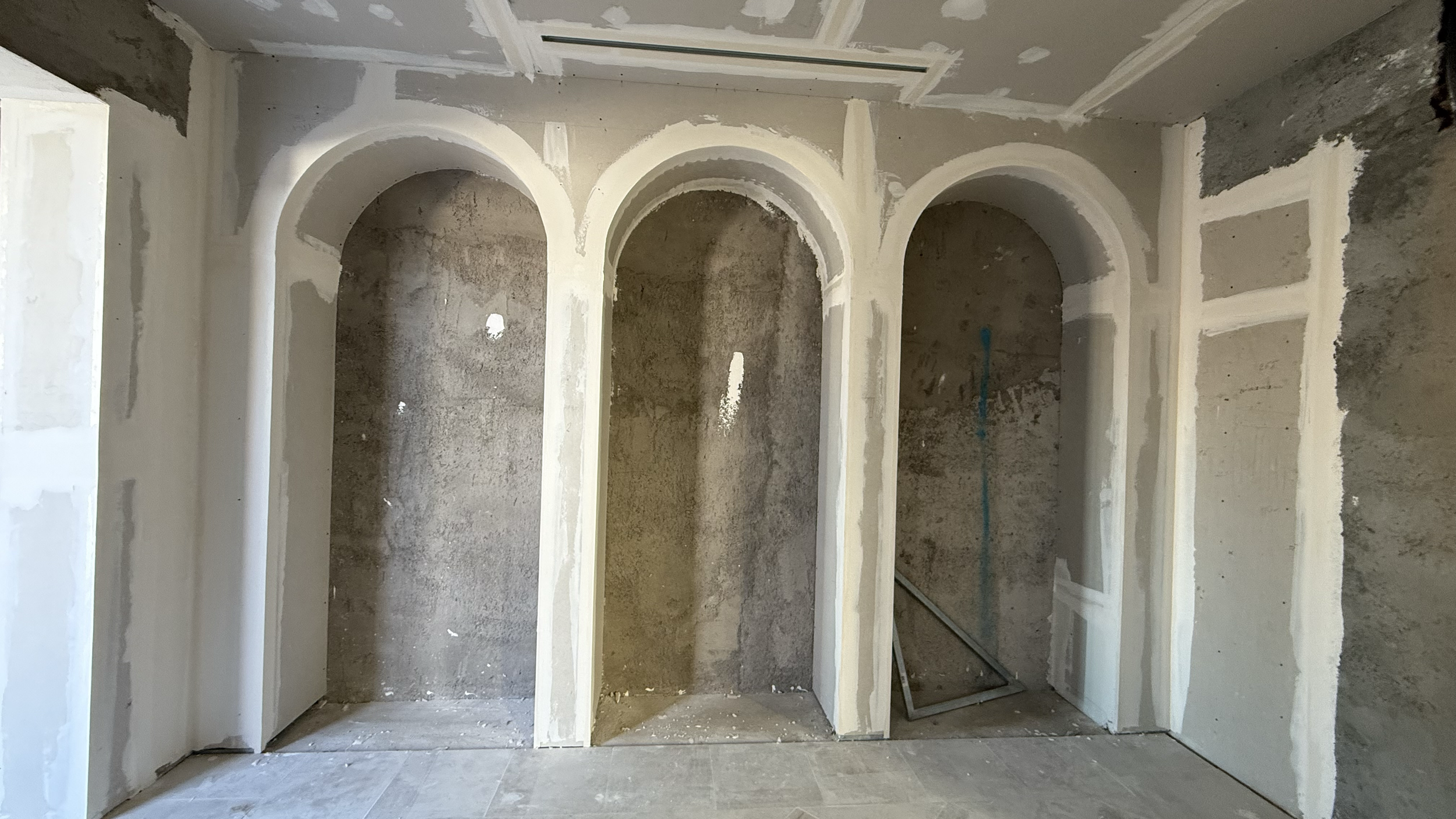 Interior of an unfinished room with three arched openings, drywall partially installed, and construction tools on the floor.