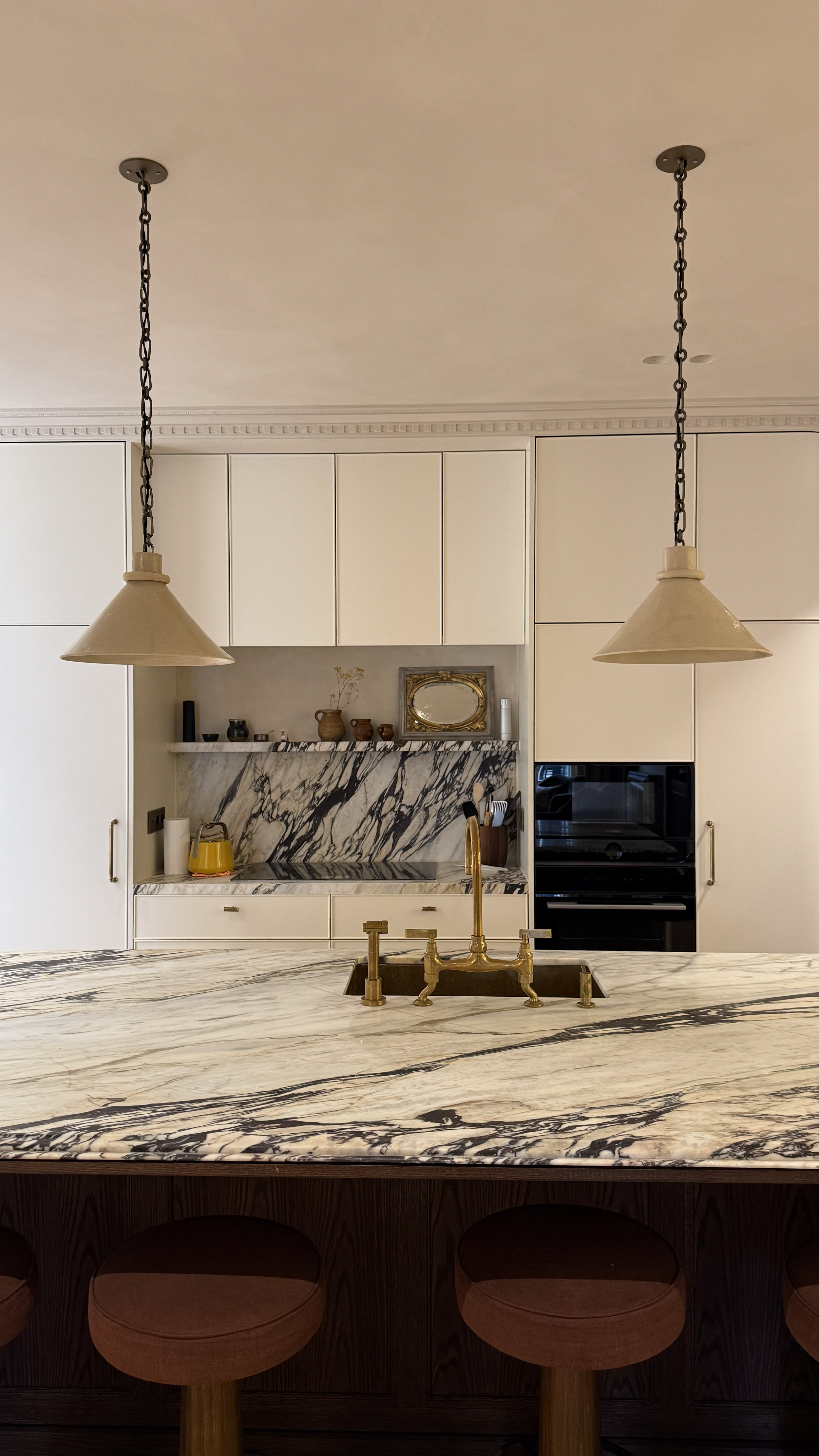 Modern kitchen with white cabinets, marble backsplash, and island with marble countertop and gold fixtures, including pendant lights and a sink.