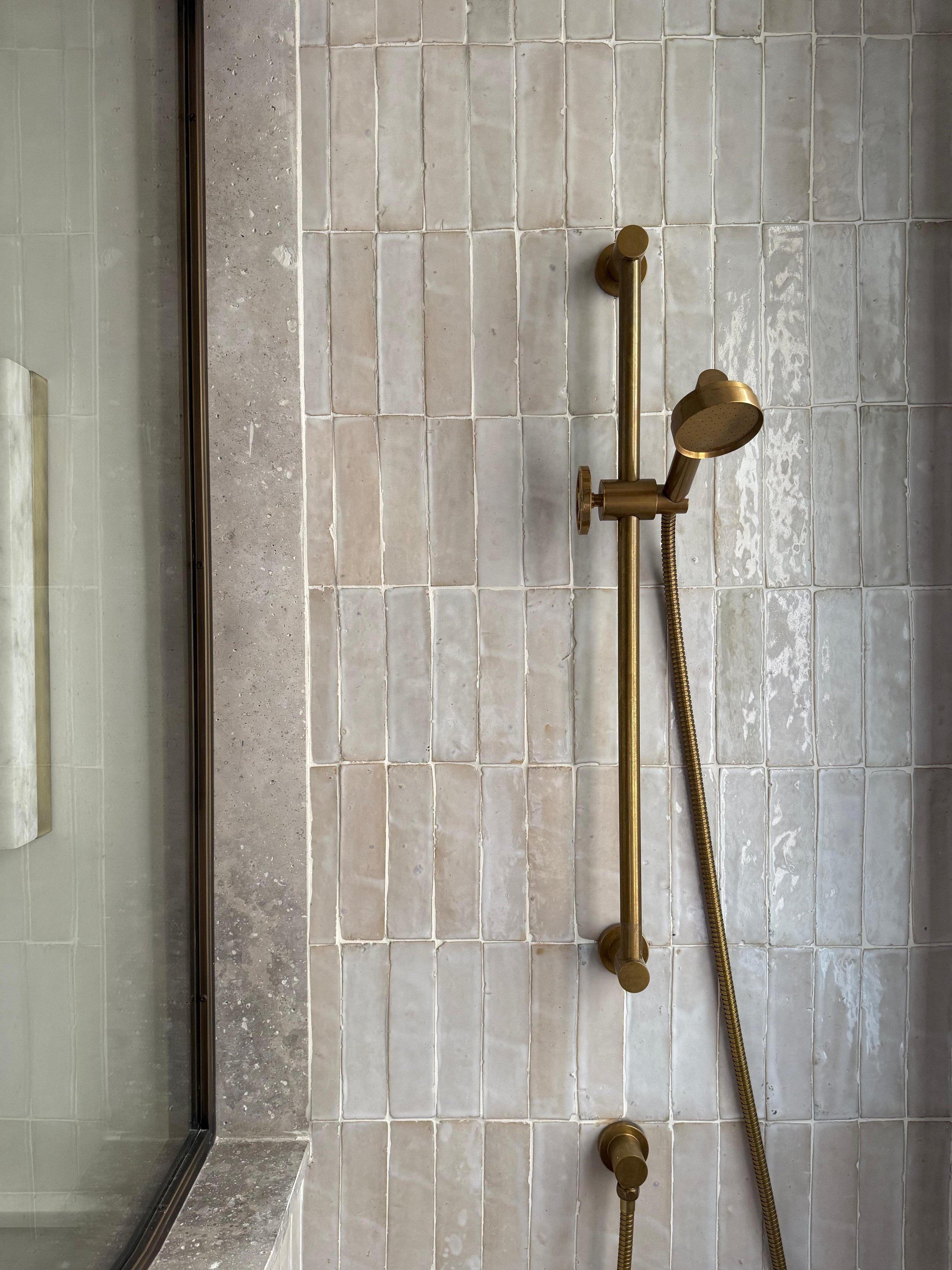 Brass shower fixtures on a tiled bathroom wall, with a glass shower door on the left.