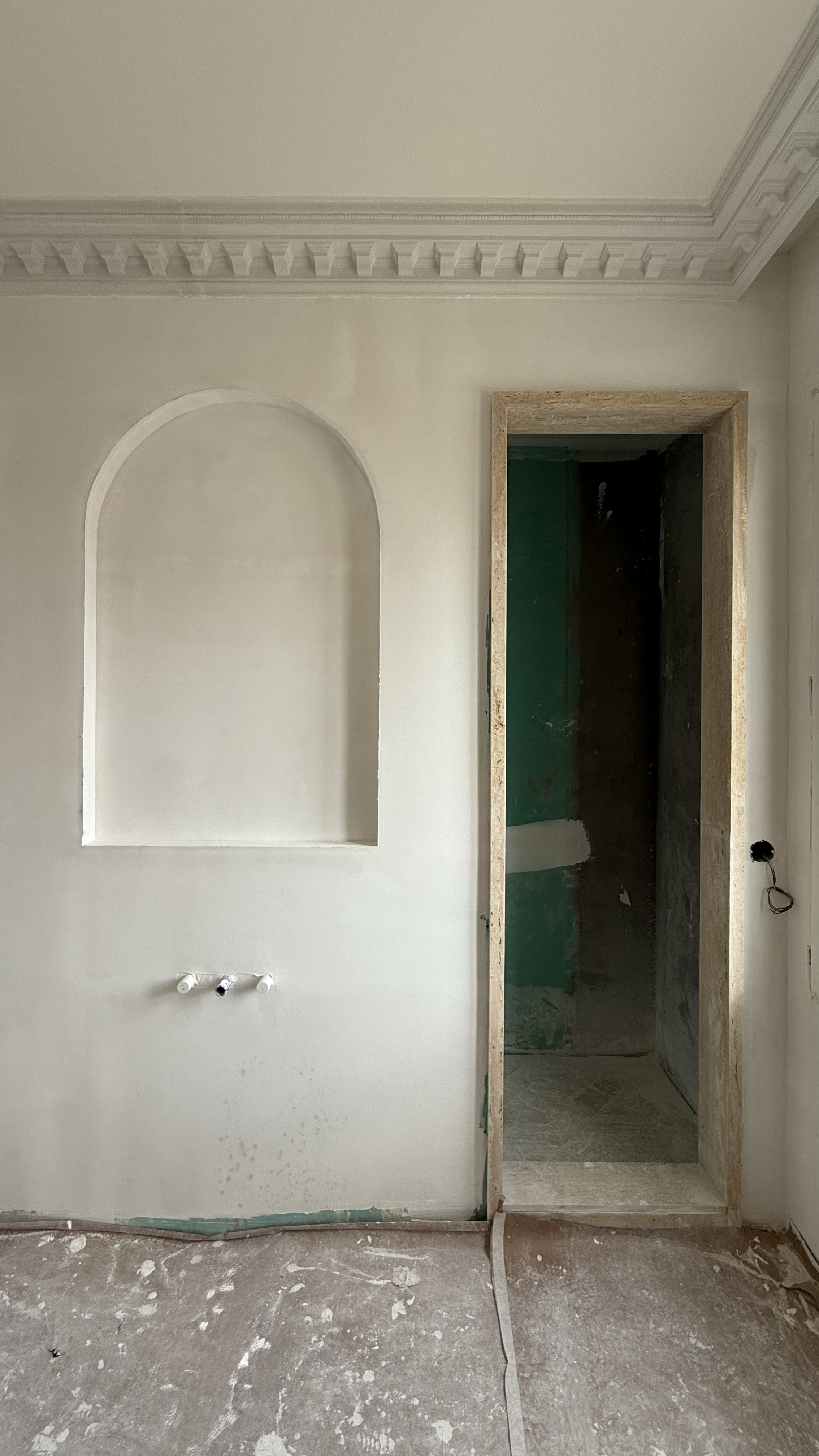 Interior of a room under construction with a decorative wall niche, an unfinished doorway, and exposed electrical wiring.