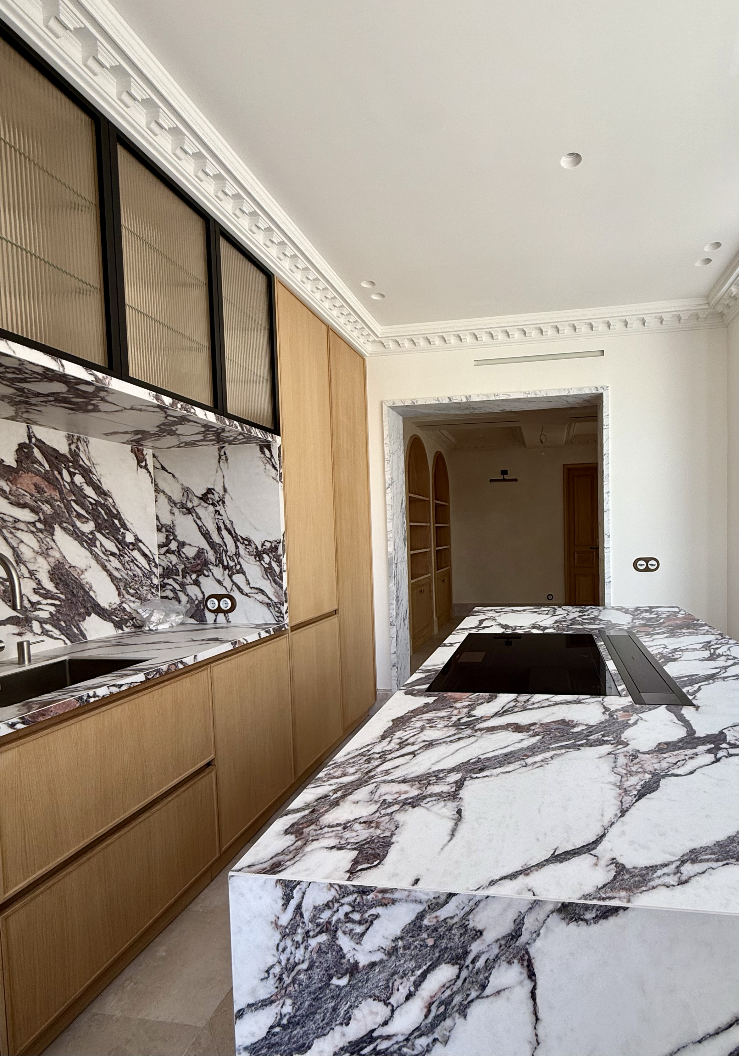 Modern kitchen with marble countertops and backsplash, wooden cabinets, and a built-in stovetop.