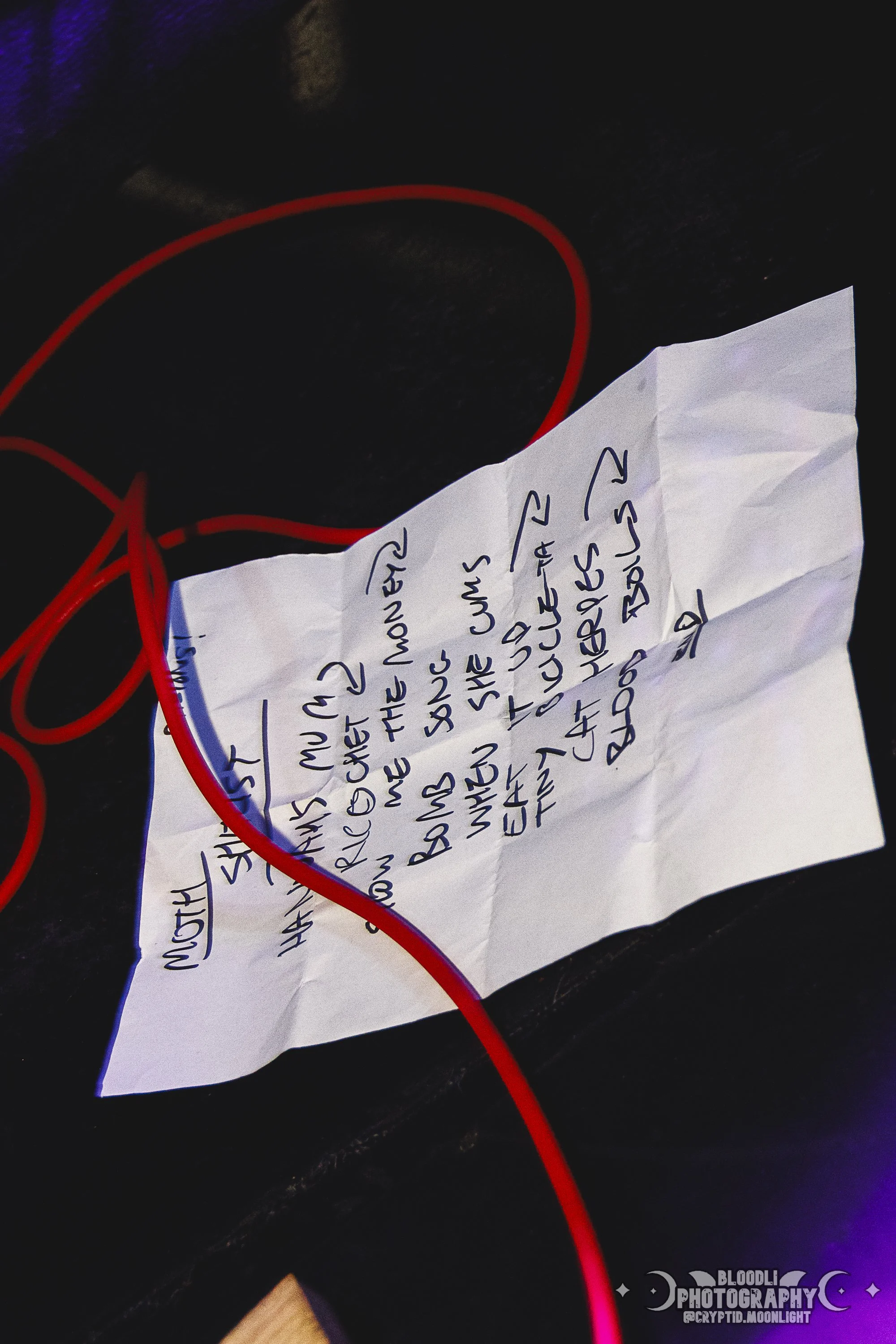 A handwritten note on crumpled paper with red headphones and a dark surface in the background, possibly a table.