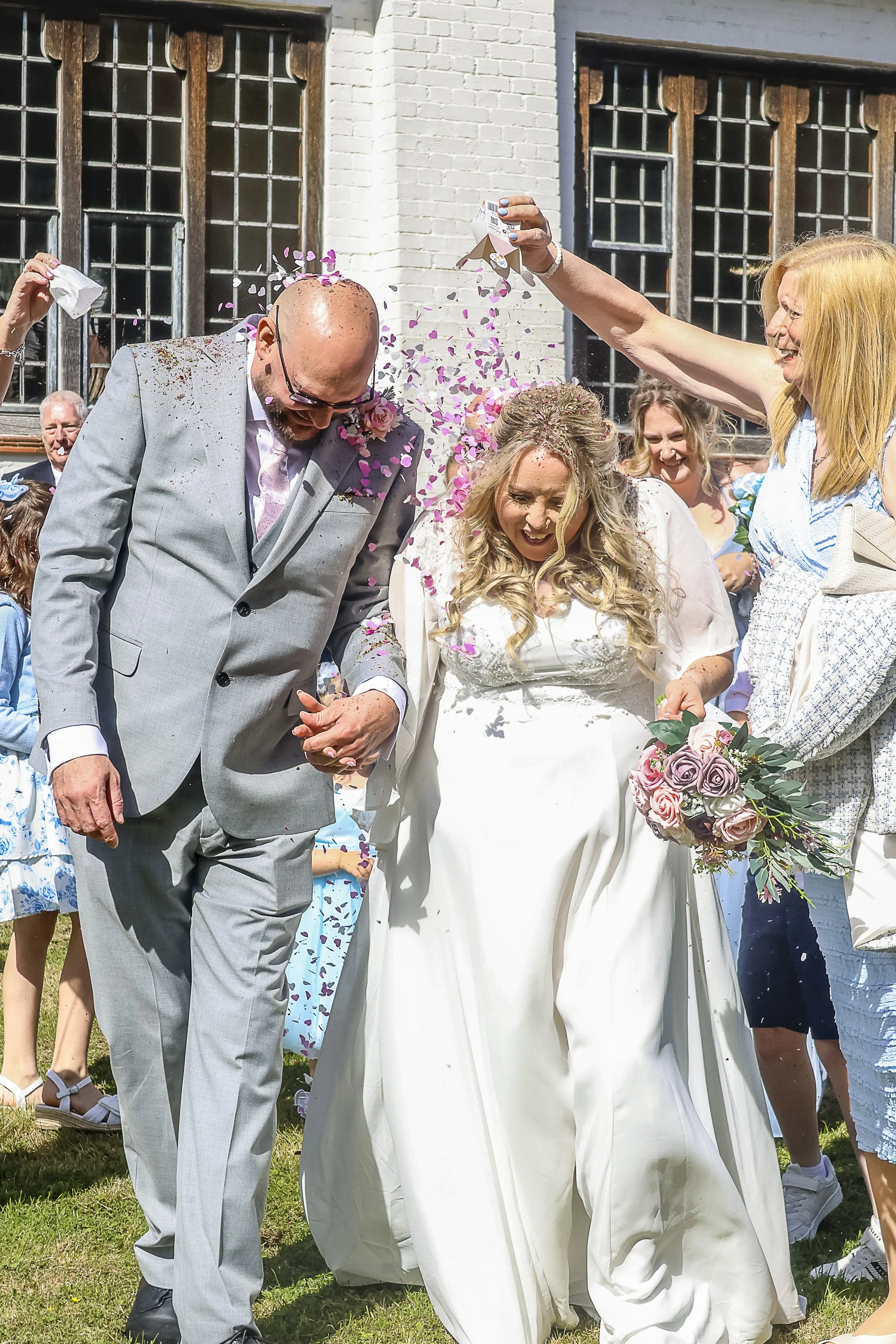A wedding celebration outdoors with a bride and groom being showered with confetti by guests.