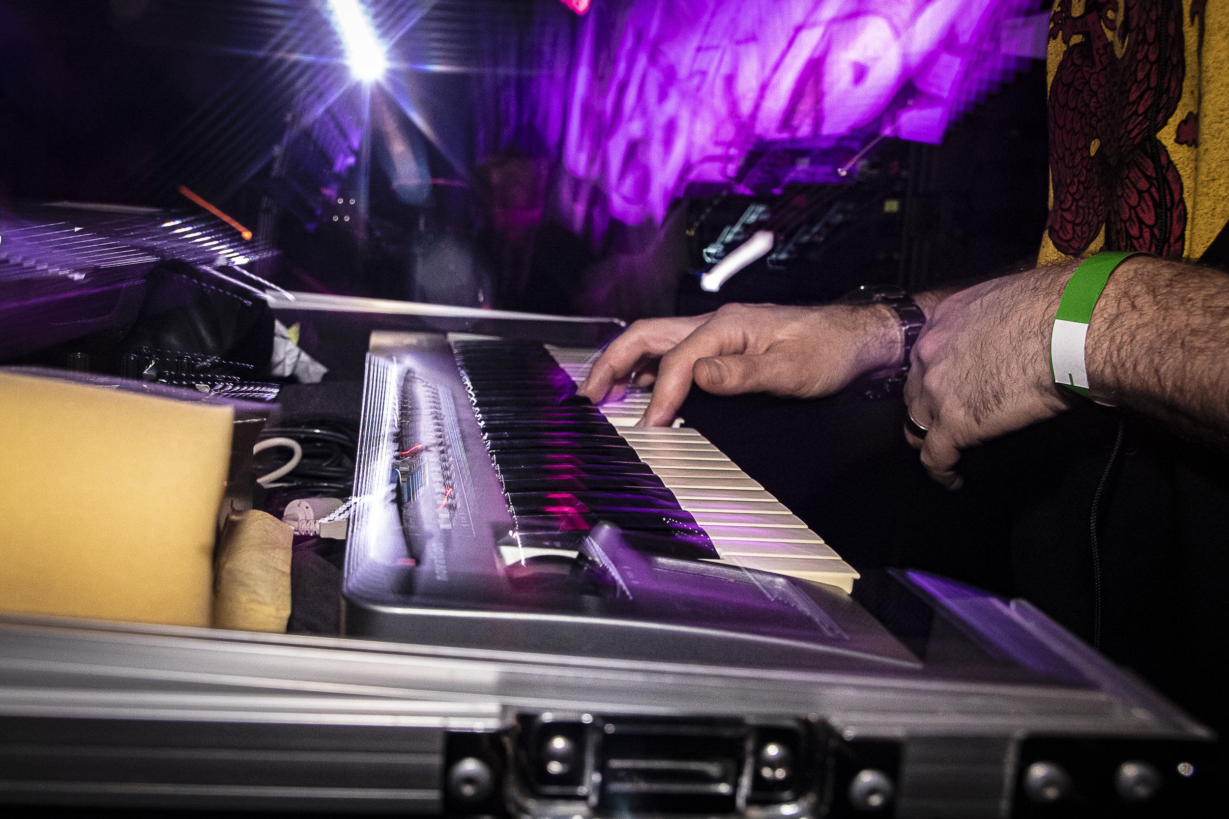 A person playing a keyboard with purple lighting and a colorful background at a live music event.