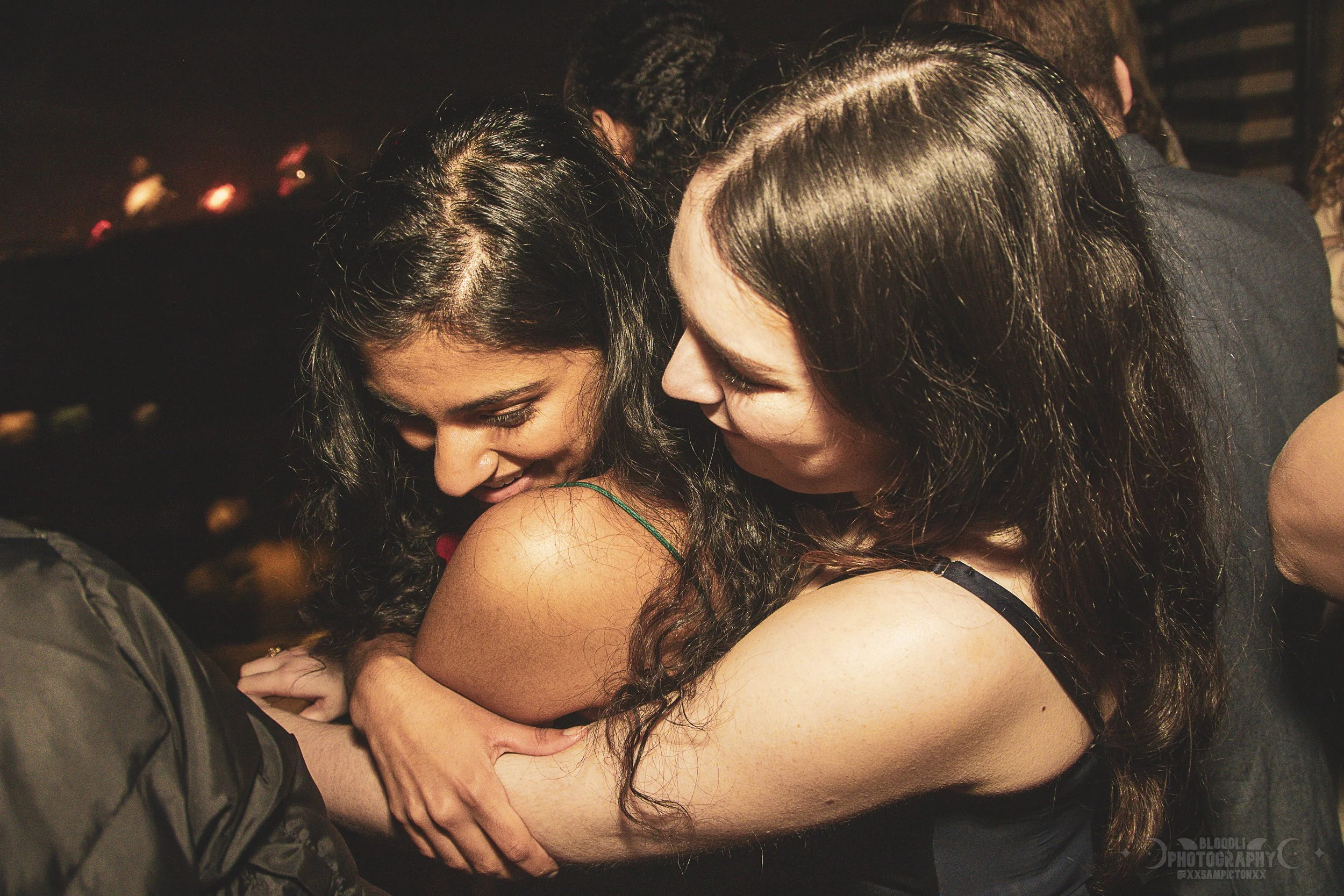 Two women hugging at a social gathering, smiling and embracing warmly.