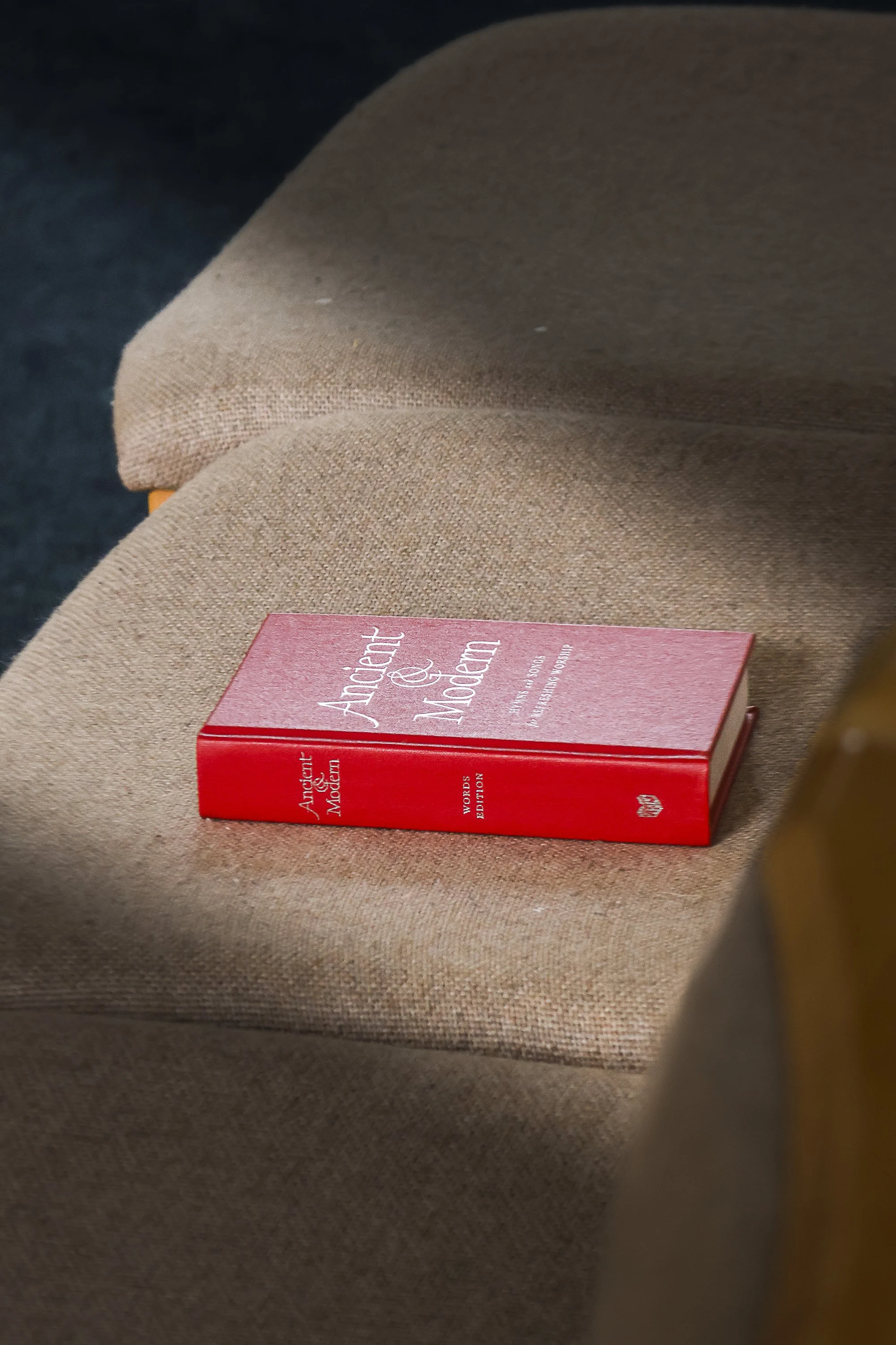 A red book titled 'Ancient & Modern' placed on a beige fabric surface.
