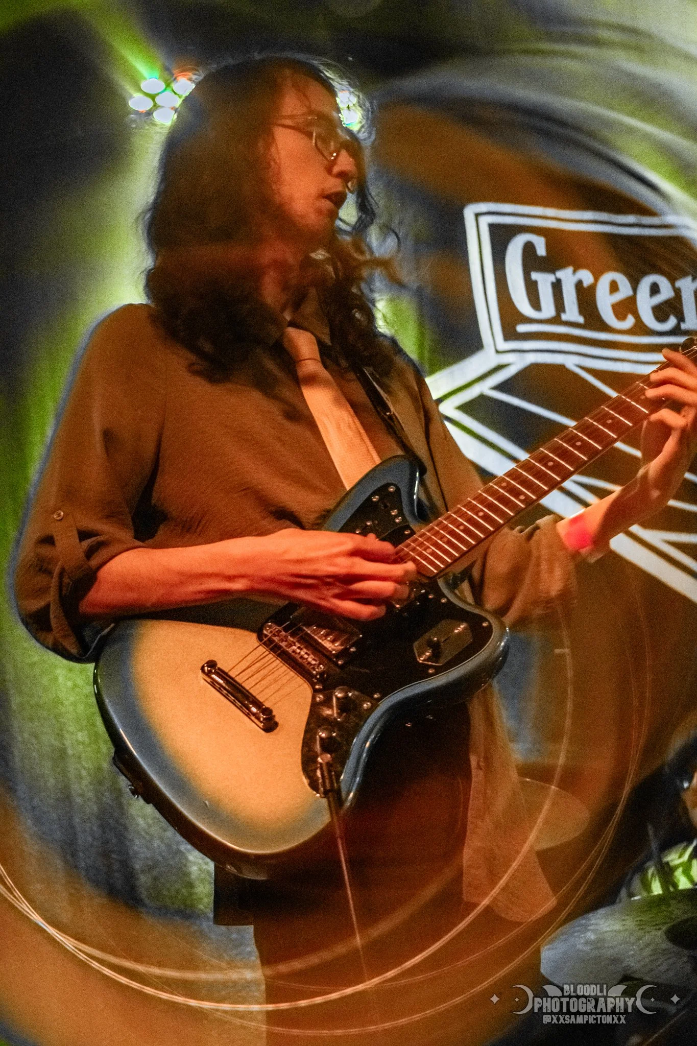 A woman with glasses playing an electric guitar on stage during a live concert.