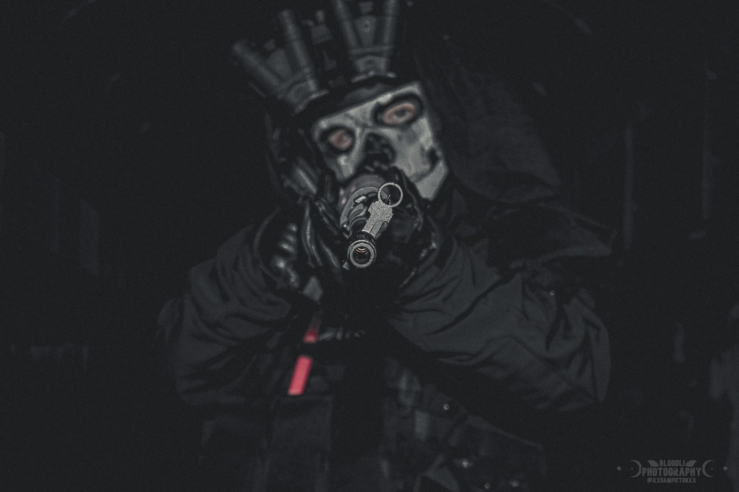 Person wearing a hockey mask and black clothing pointing a gun toward the camera in a dark environment.
