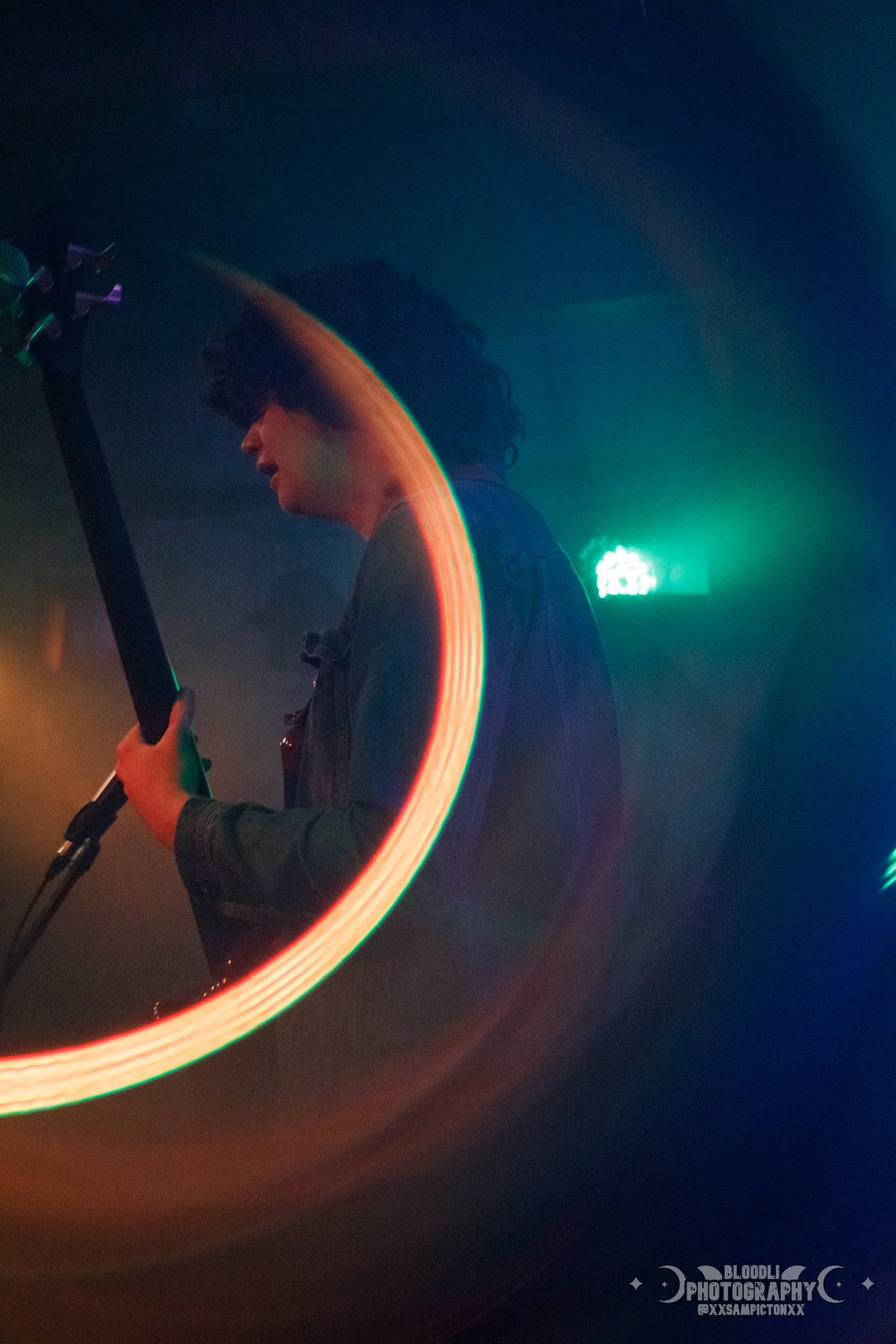 A woman with curly hair on stage, illuminated by colorful lights, playing an electric guitar near a microphone.