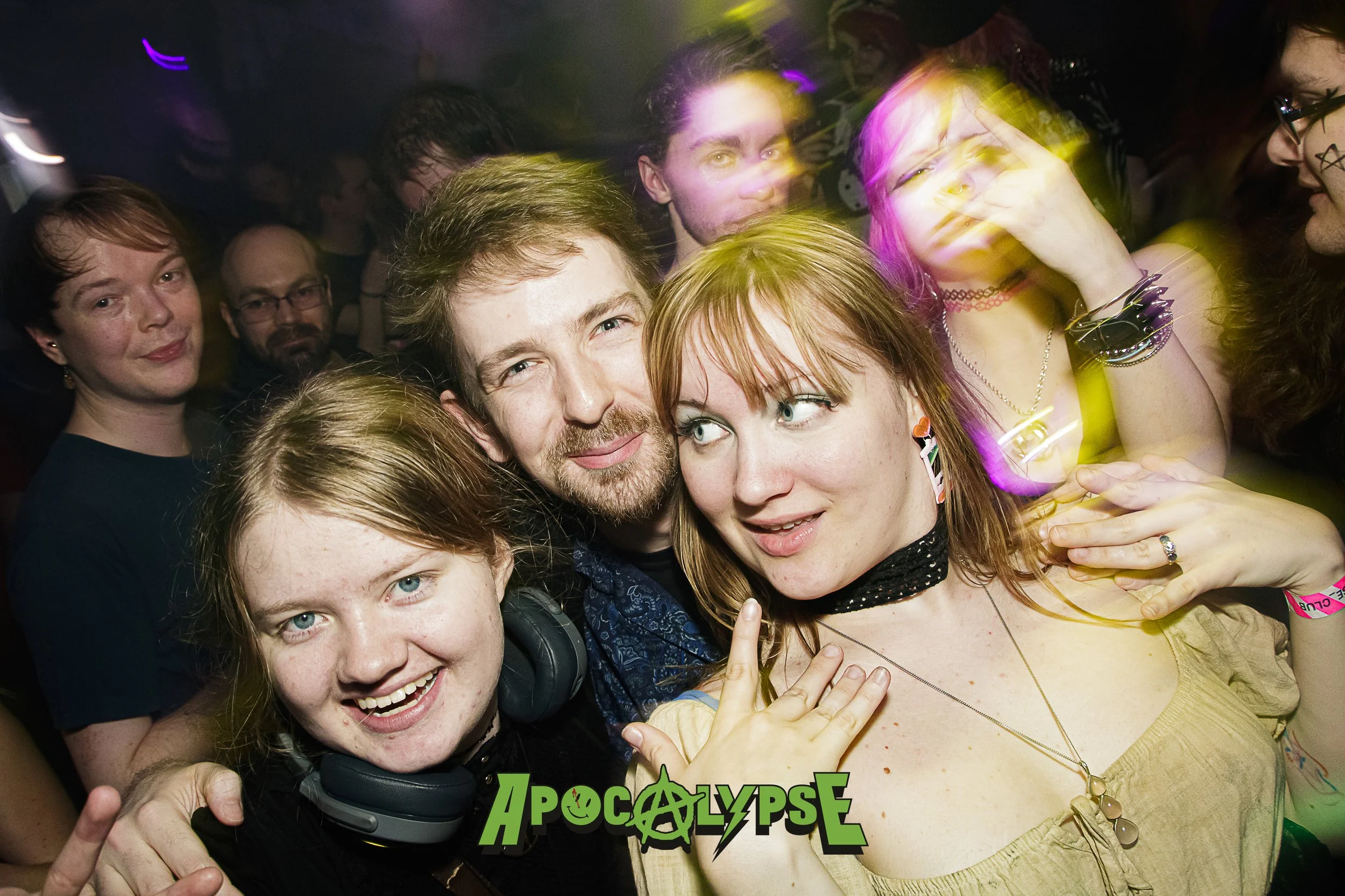 People at a crowded party or concert, some smiling and some making playful gestures, with colorful lighting.