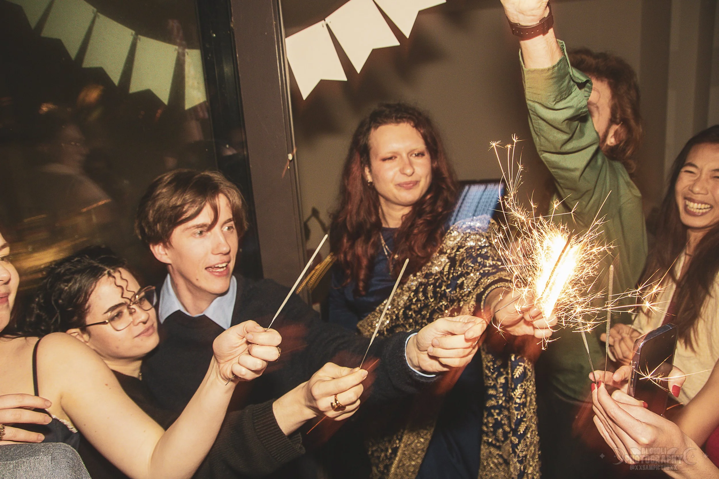 Group of friends celebrating with sparklers at a party, smiling and having a good time.