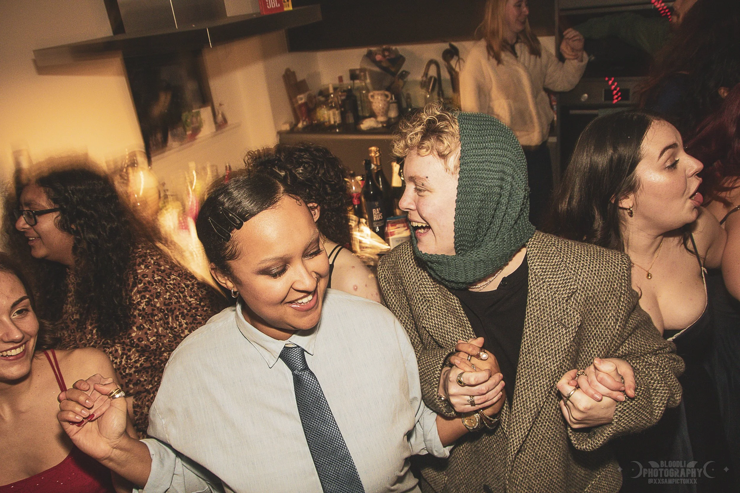Group of people dancing and enjoying themselves at a party, with some holding hands and smiling.
