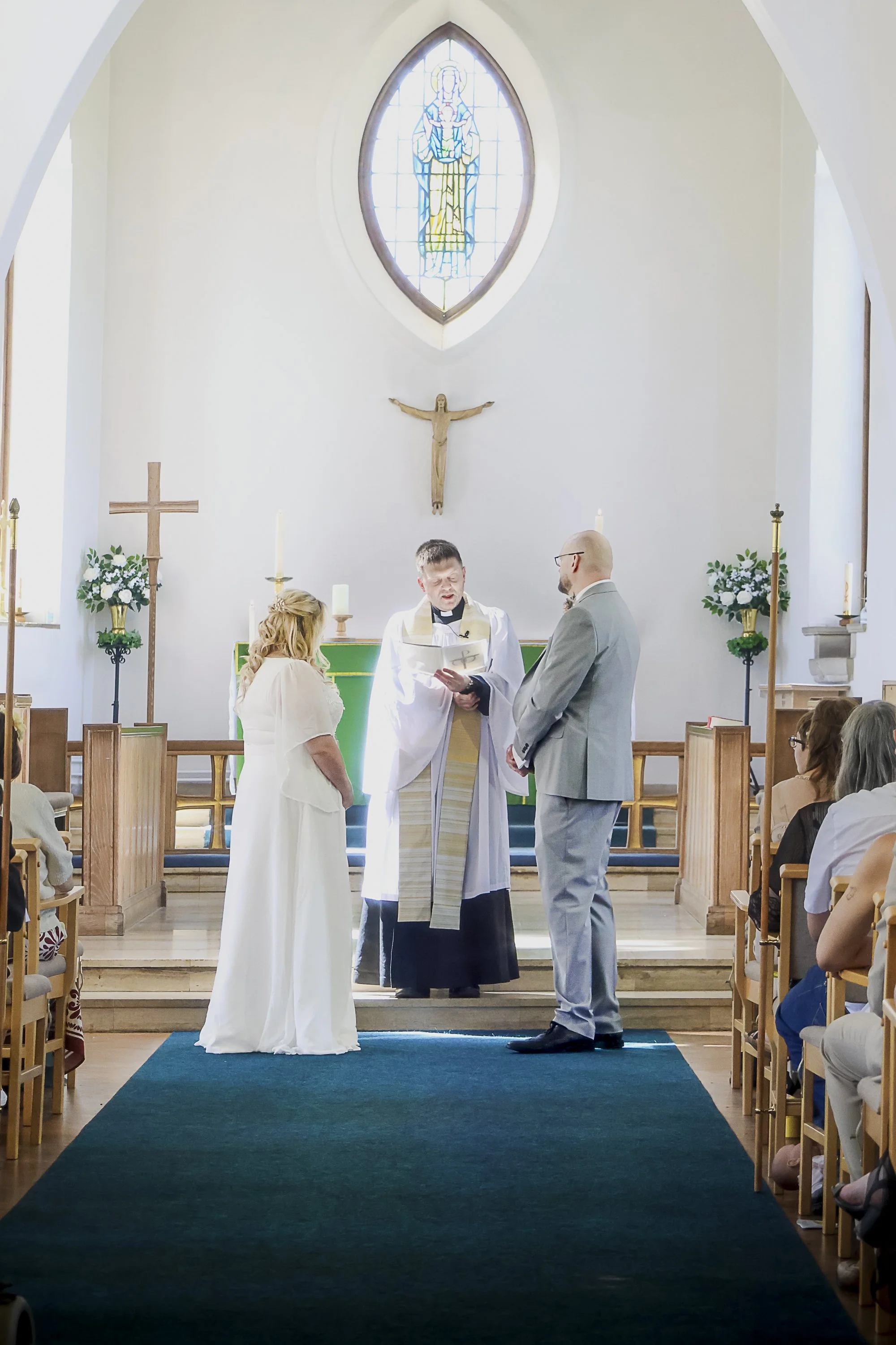 A wedding ceremony taking place in a church with a priest, a bride, and a groom standing before the altar.