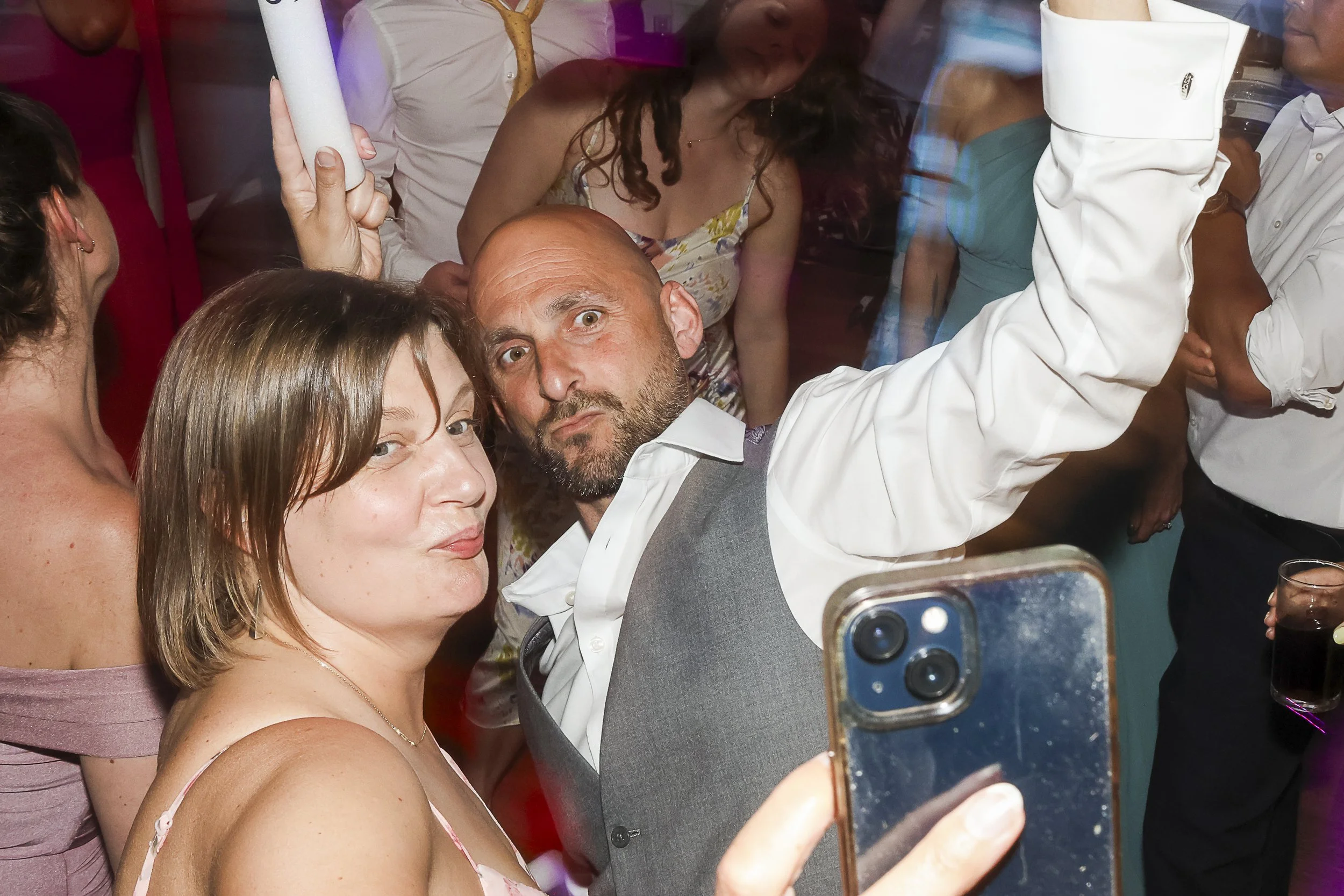 Group of people taking a selfie at a party or celebration, with colorful lighting and drinks visible.