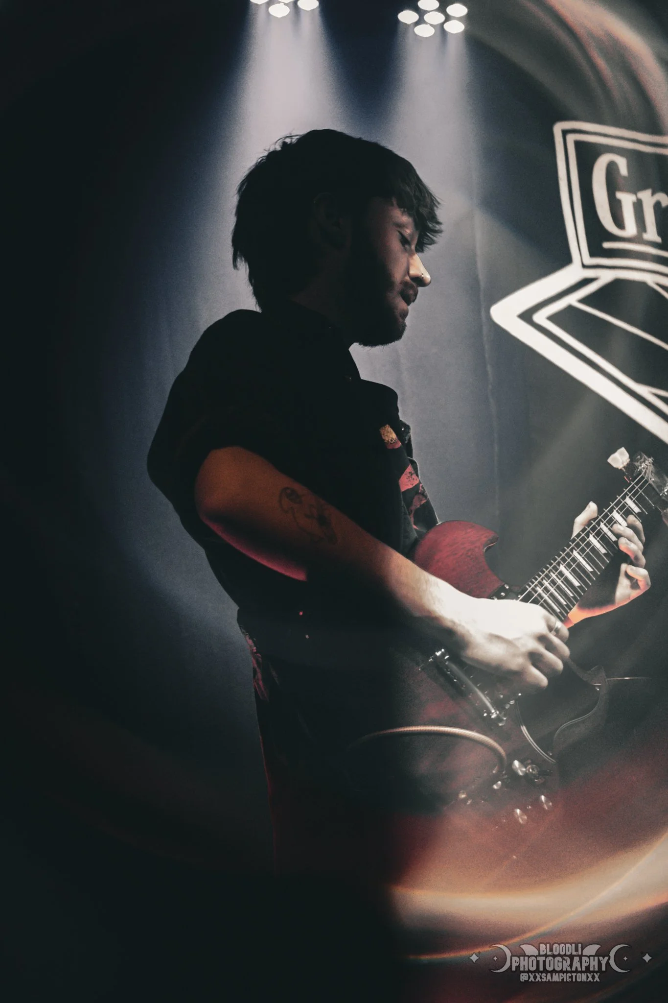 A person playing an electric guitar on stage with a dark background and stage lights shining down.