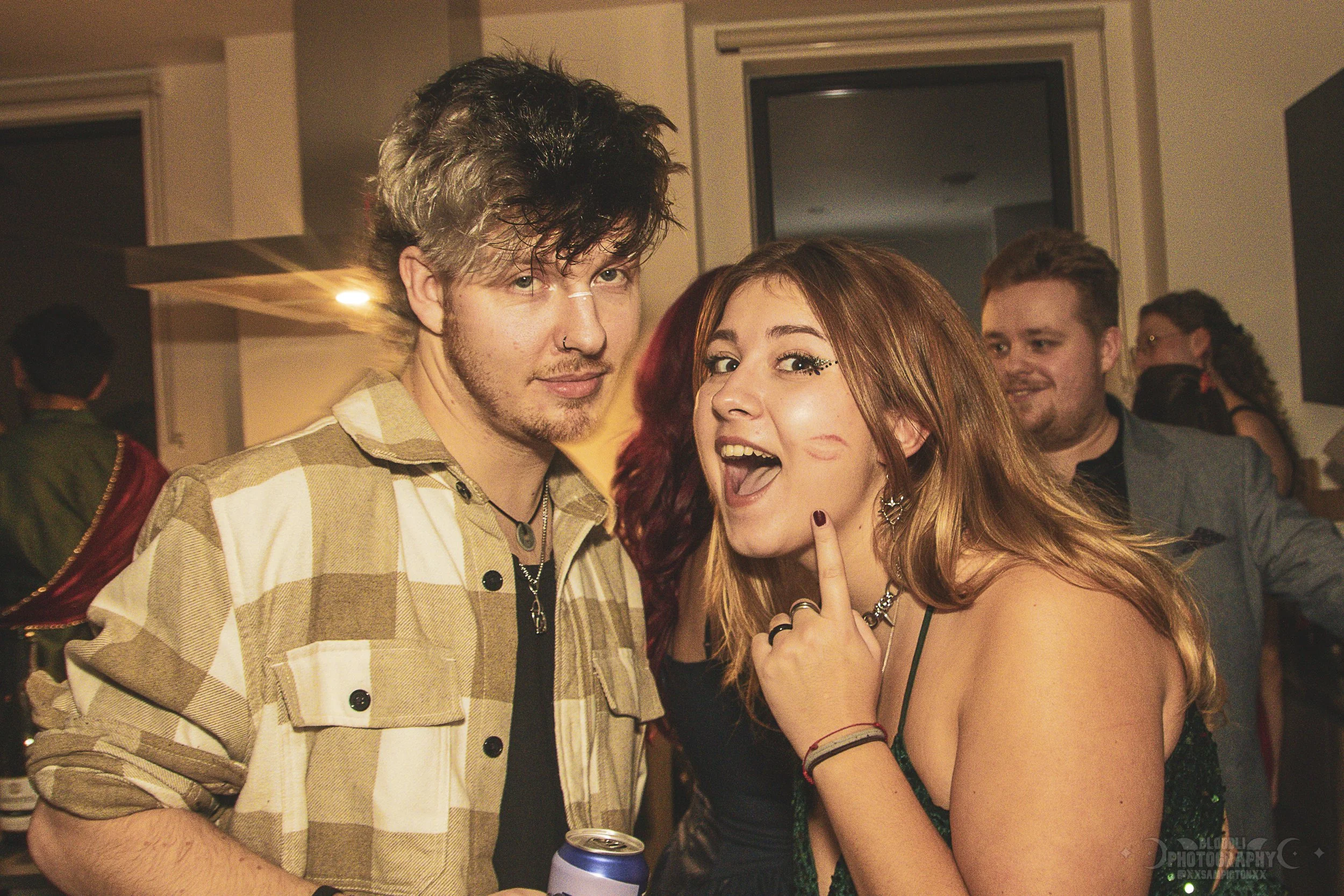 Young man and woman at a party, the woman is pointing to her cheek with a playful expression.