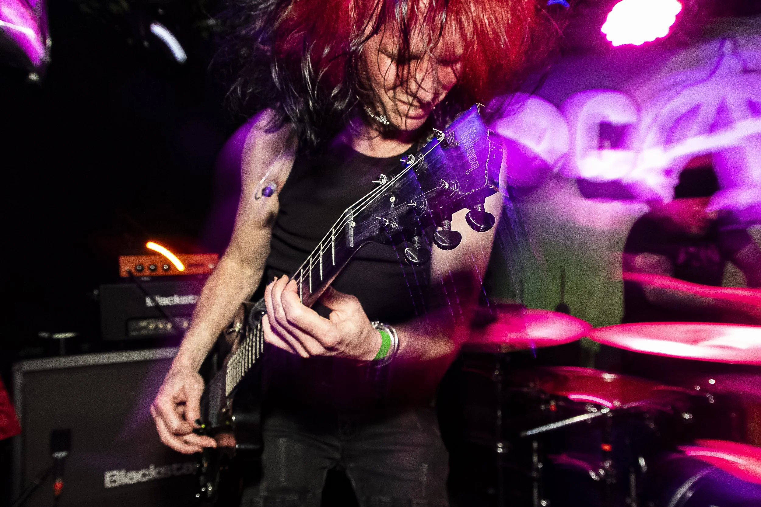 A person playing an electric guitar on stage with colorful lighting effects.
