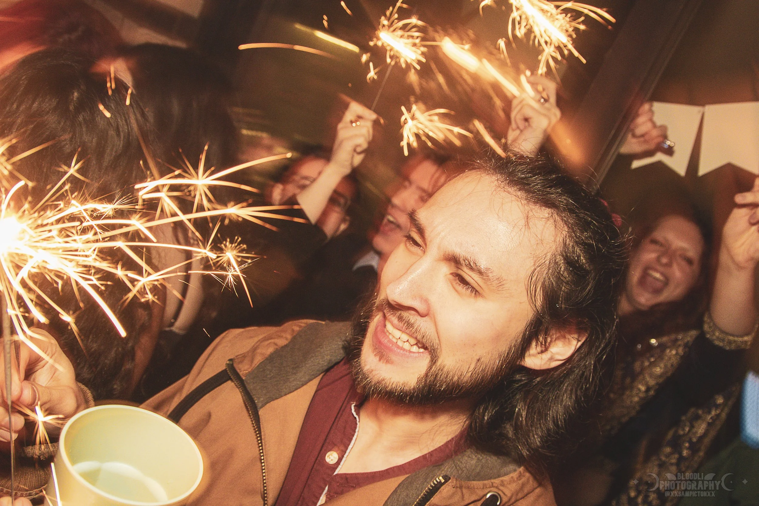 People celebrating with sparklers and party hats at a festive gathering.