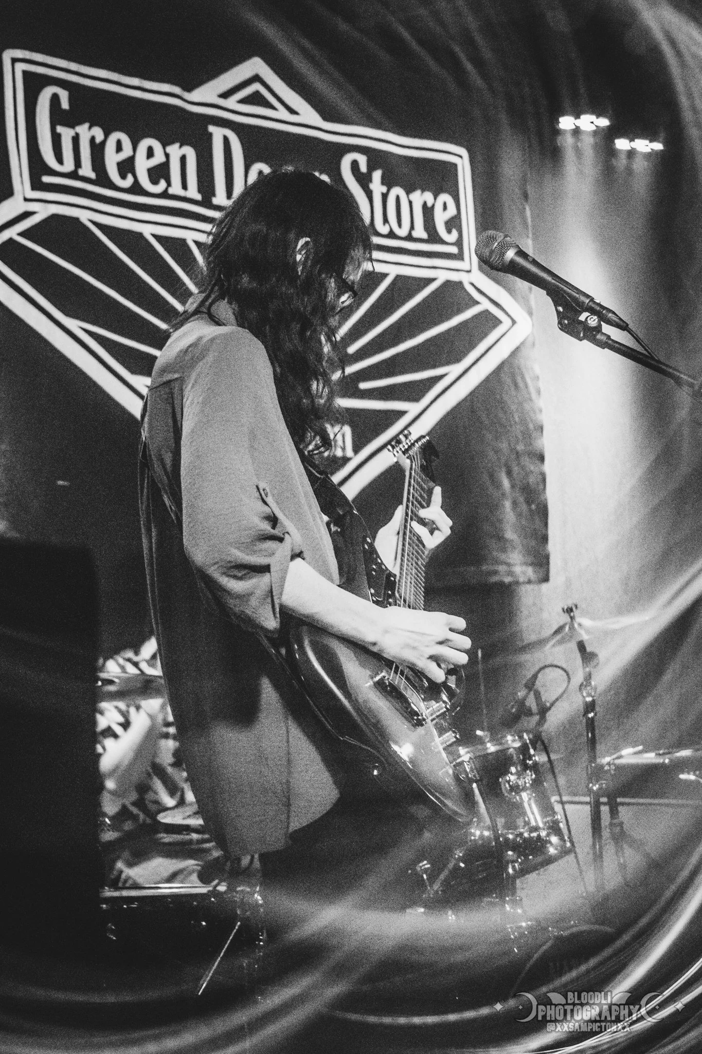 A woman playing an electric guitar on stage in front of a sign that reads 'Green Day Store' at night during a live performance.